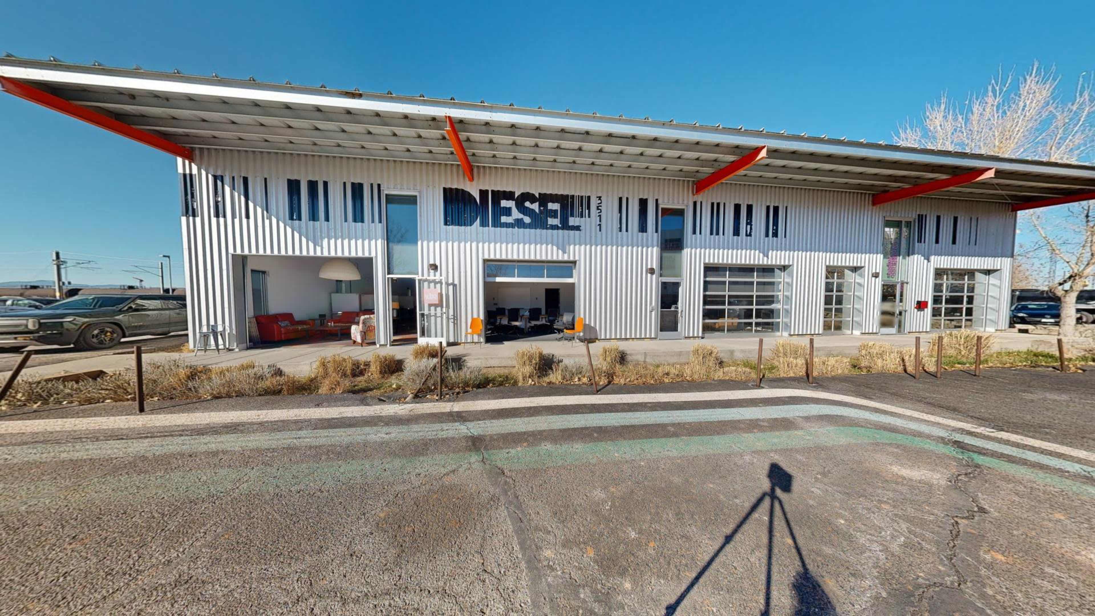 The image shows a modern, industrial-style building with large windows, a prominent sign reading "DIESEL," and a landscaped area in front.
