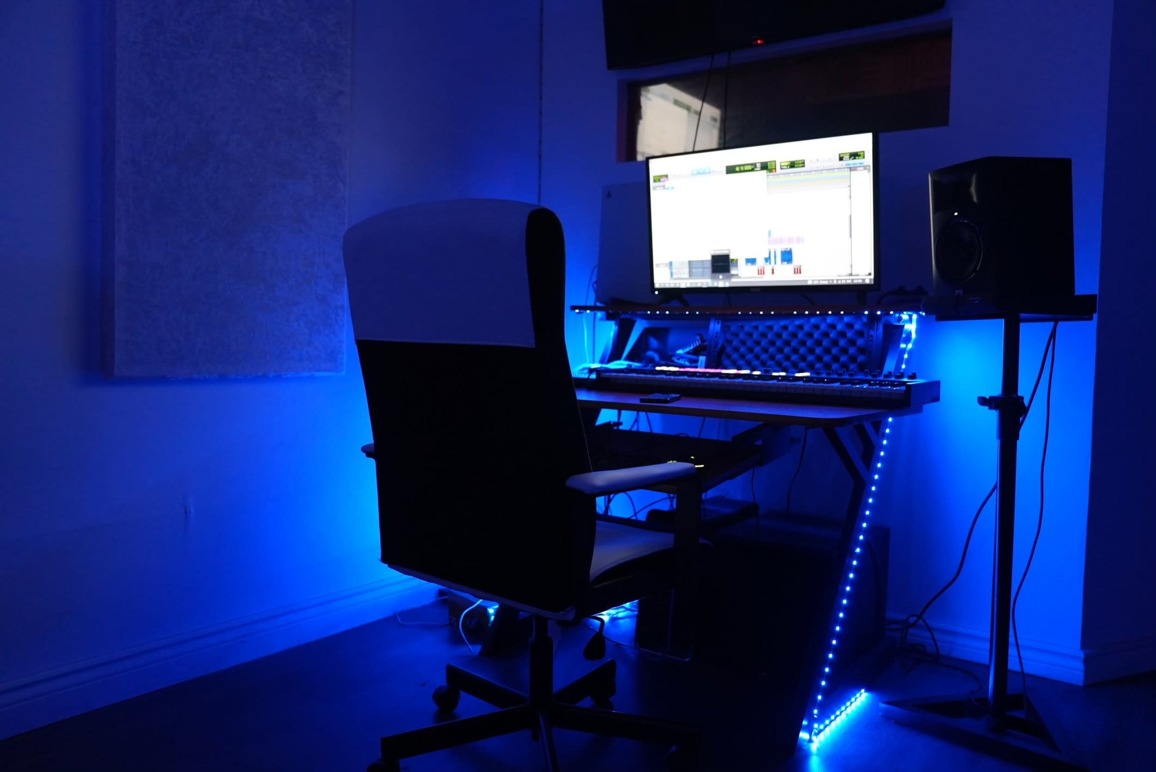 A music production workspace features a computer monitor, keyboard, and speakers illuminated by blue LED lights.