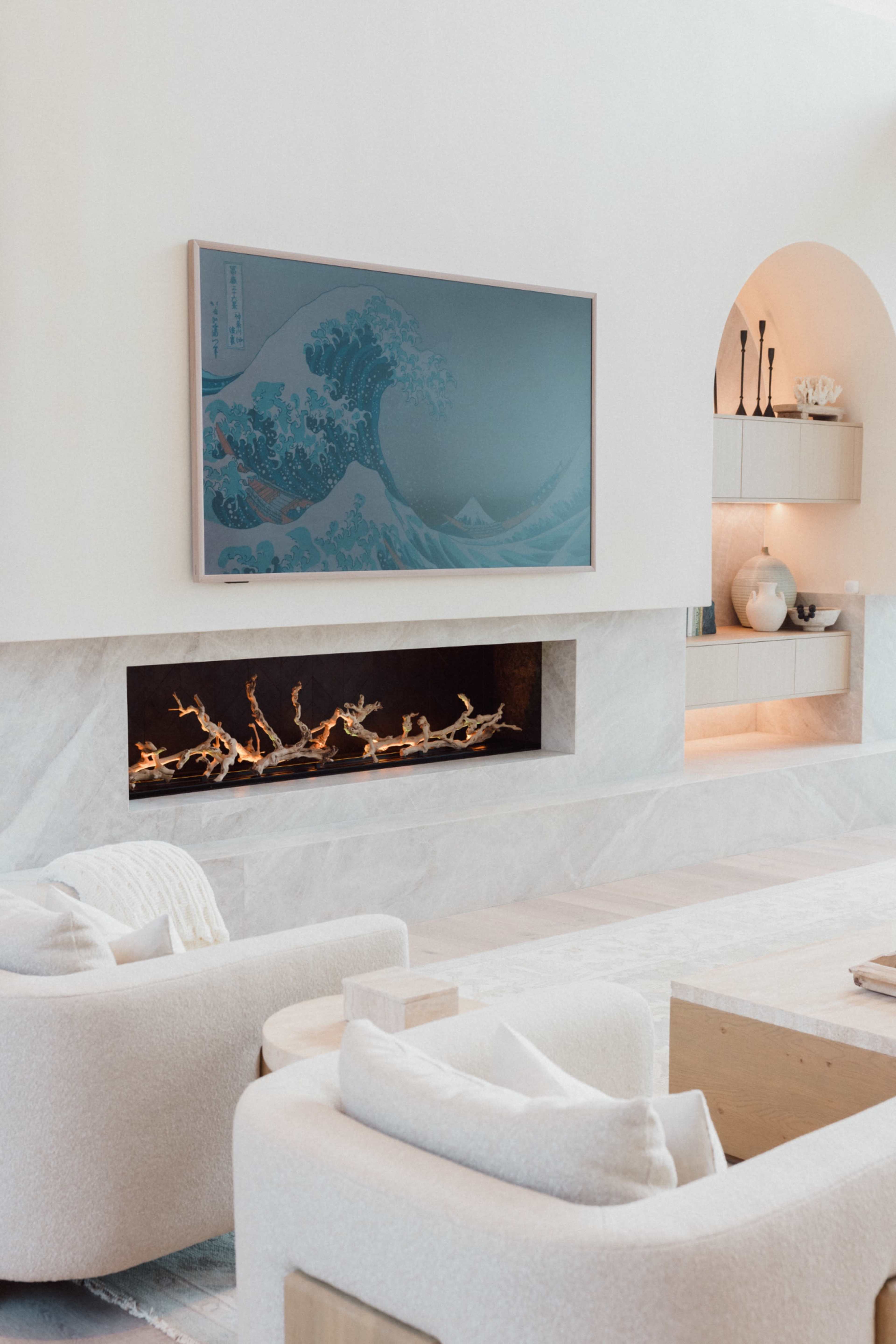A modern living room features a wall-mounted artwork depicting a wave, with a minimalist fireplace built into a marble wall.