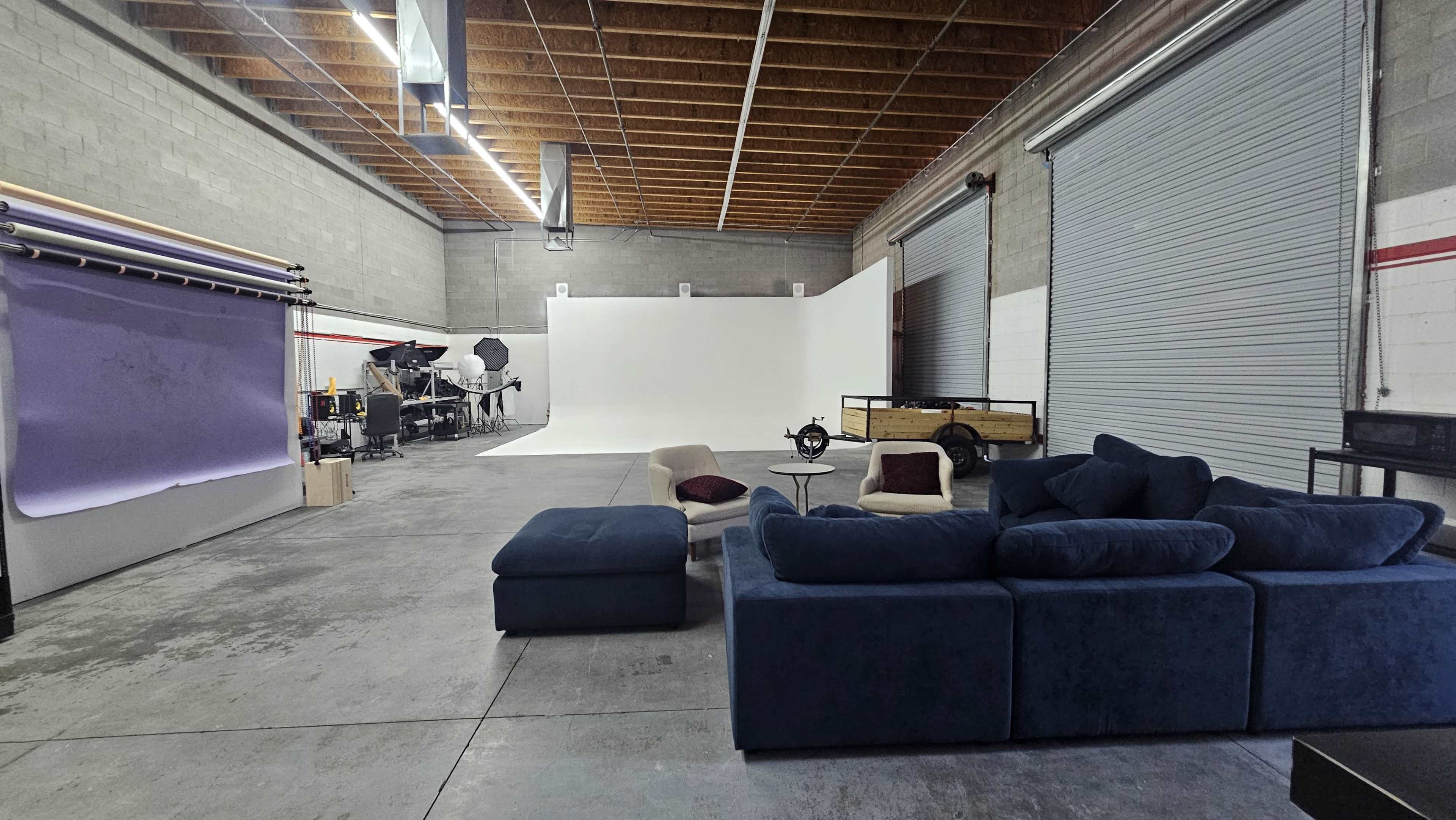 The image shows a spacious studio setup featuring a sectional couch, a blank white backdrop, and photography equipment in the background.