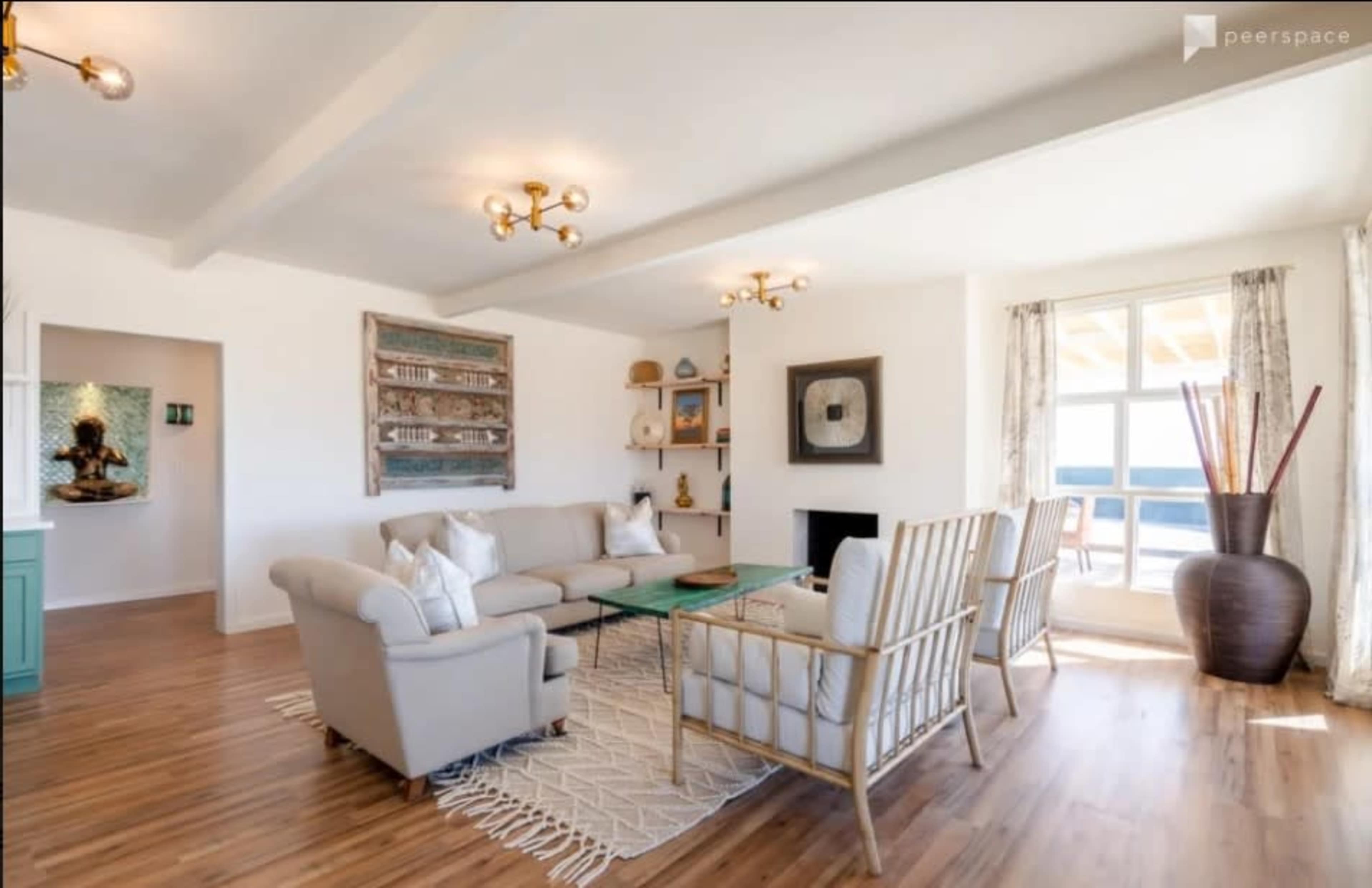 A light-colored living room with a sofa, armchairs, a coffee table, and large windows overlooking a view.