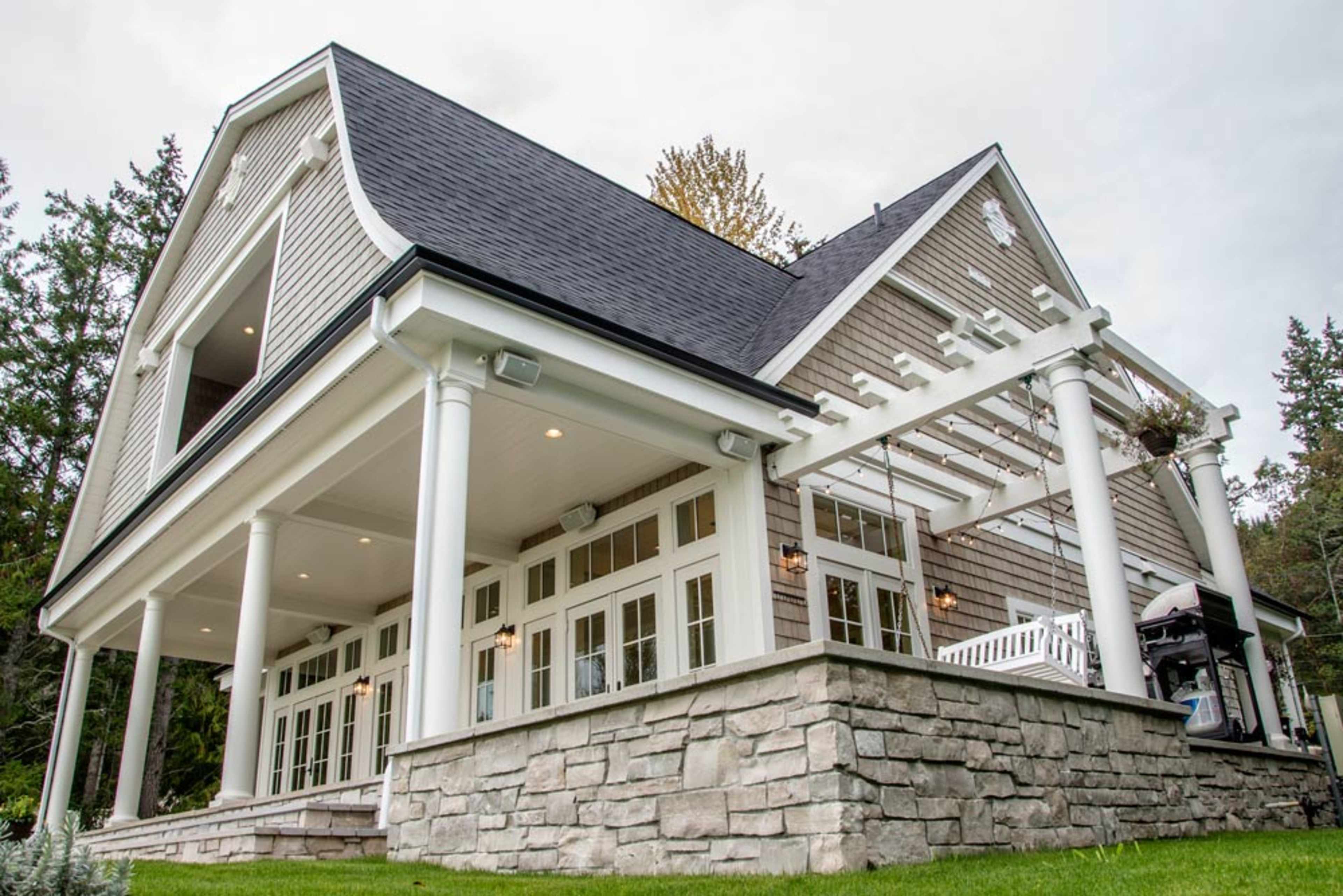 A modern house with a sloped roof, stone foundation, and a series of large windows and doors on the ground floor.