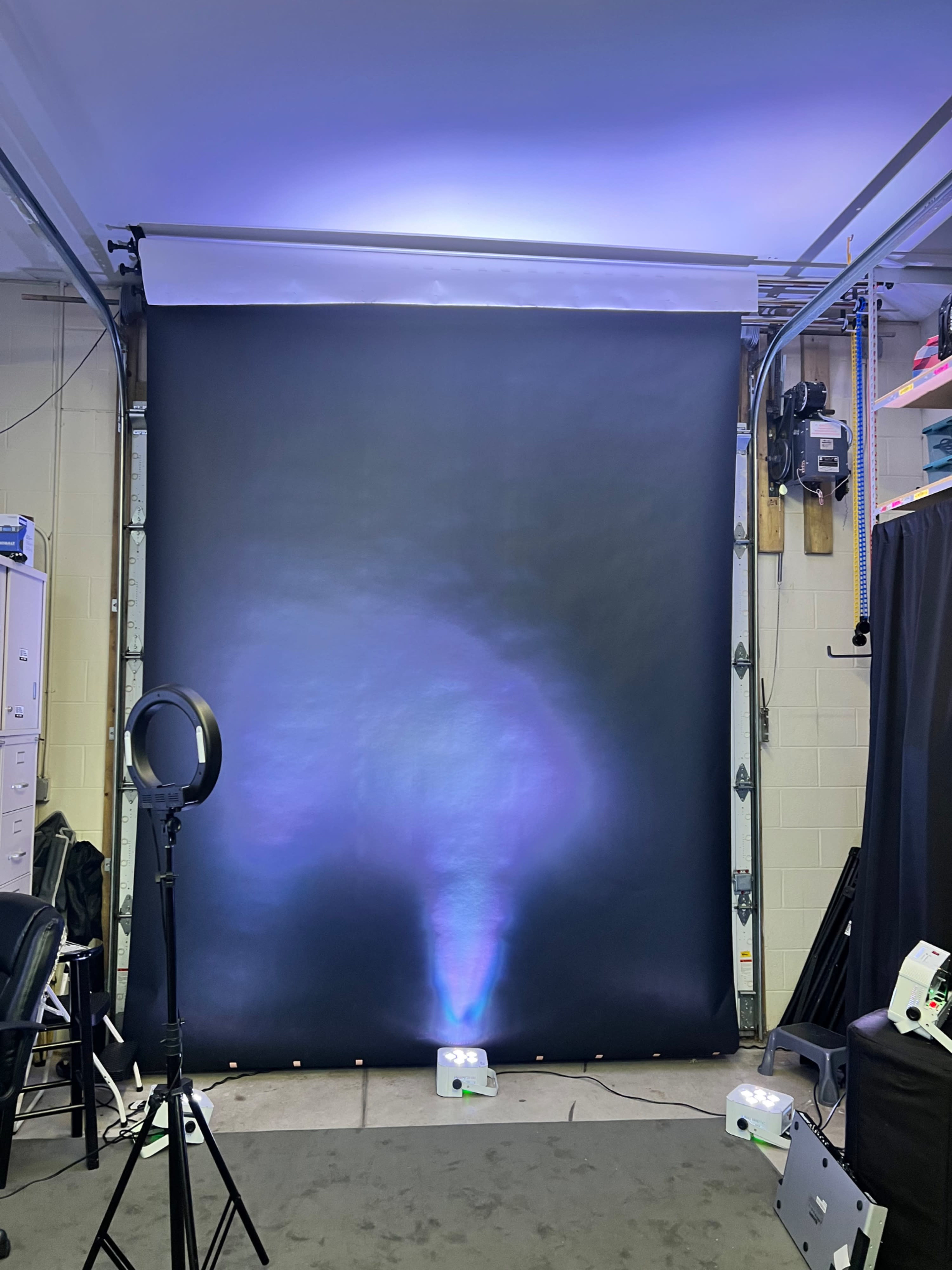 A studio setup with a black backdrop, a ring light on the left, and a projector emitting light onto the backdrop.