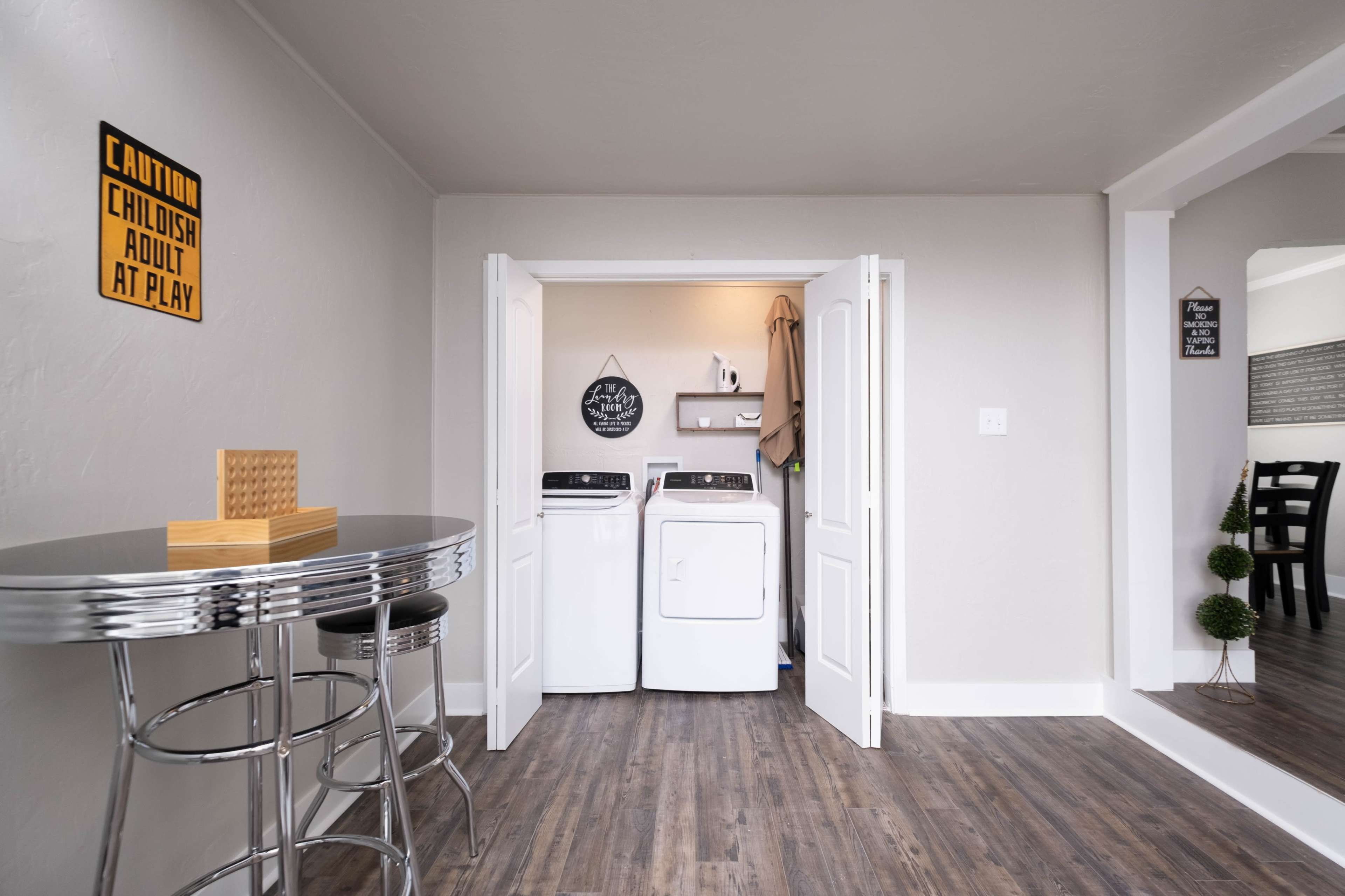 A small laundry area is visible through double doors, featuring a washer and dryer, alongside a round table with stools in a light-colored room.