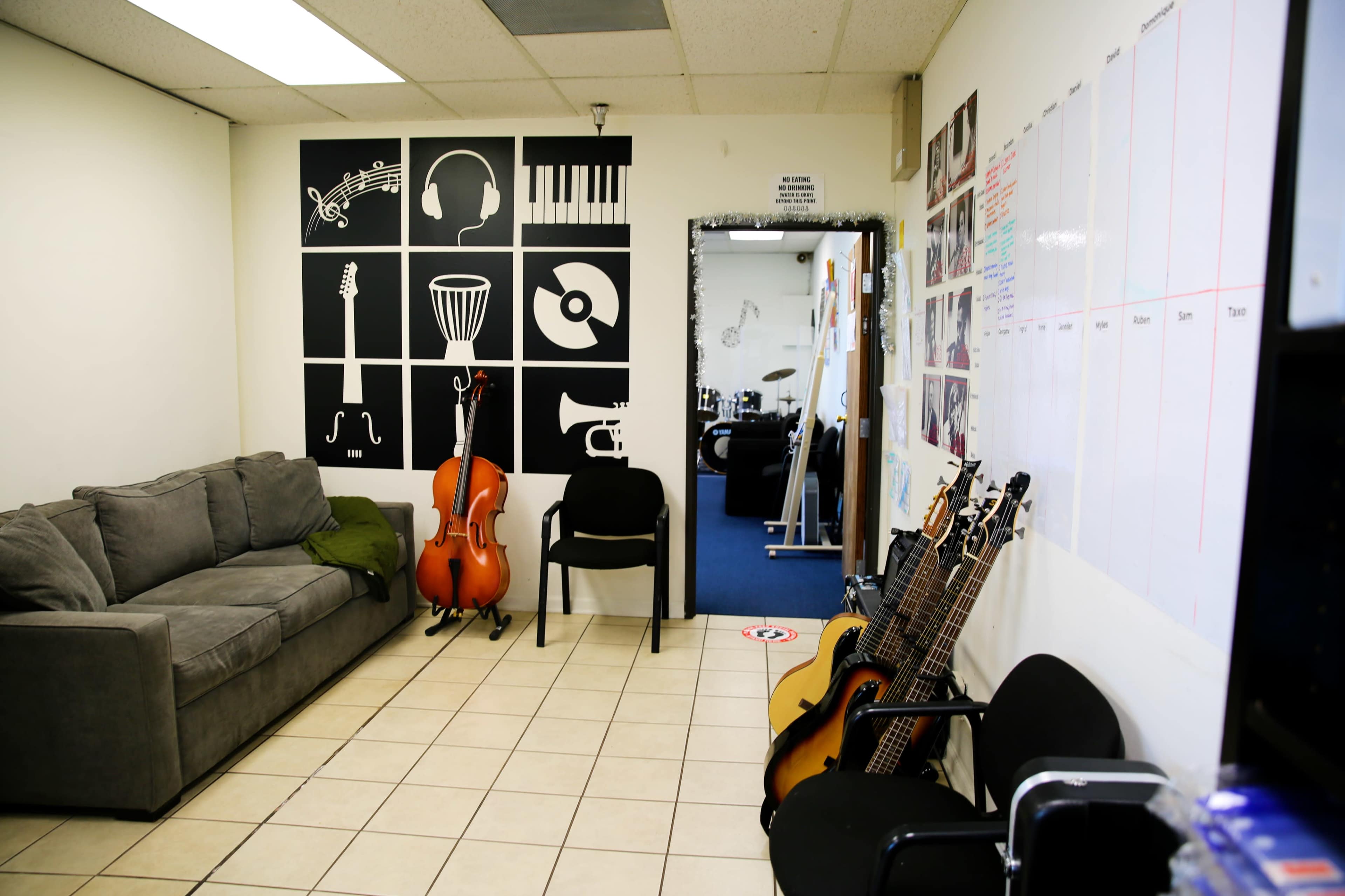 A music studio features a gray couch, a cello, and several guitars against walls adorned with musical-themed graphics.