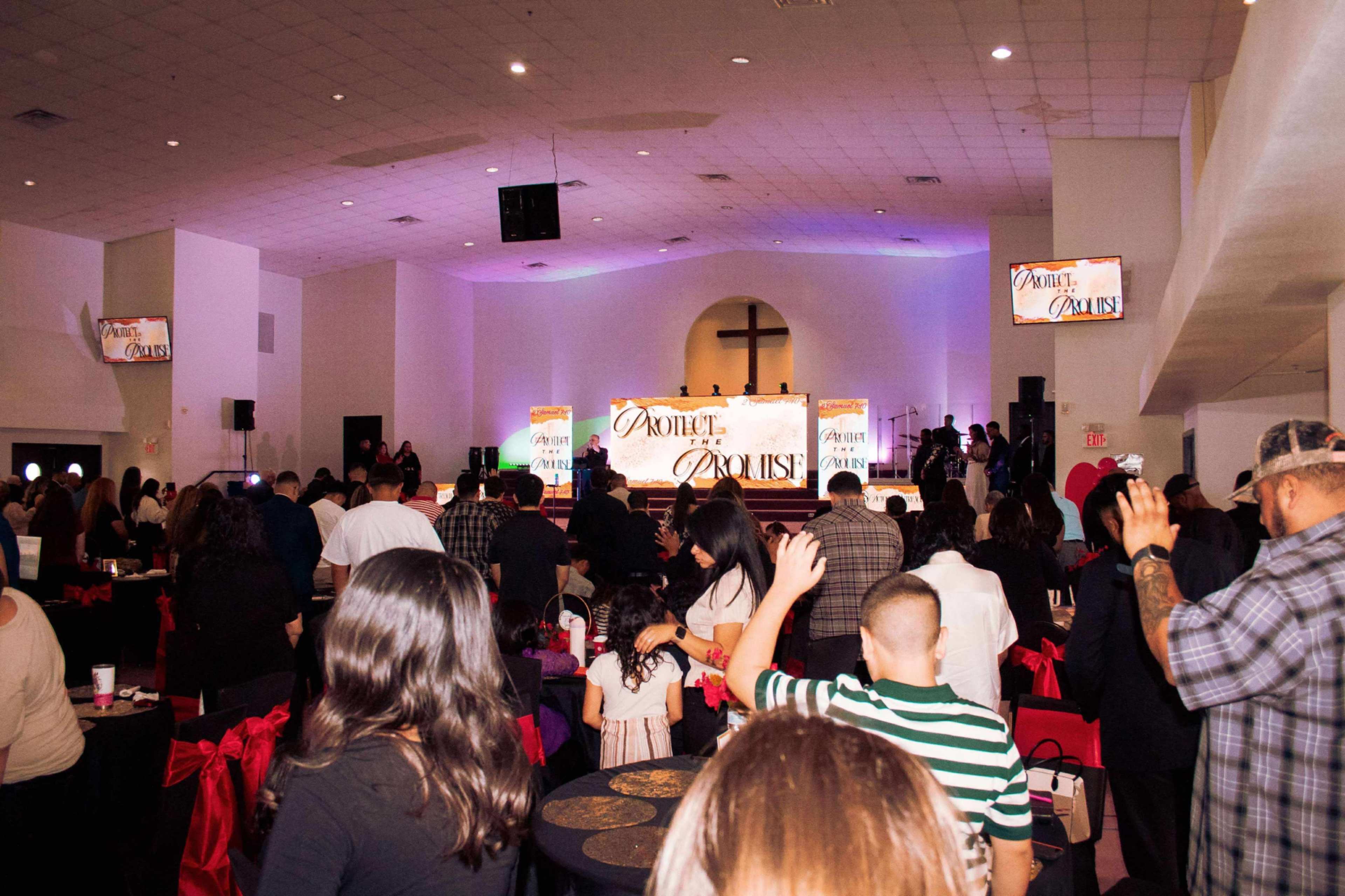 A group of people is gathered in a large indoor space, some with raised hands, in front of a stage displaying a large sign with the text "DAUNTLESS."
