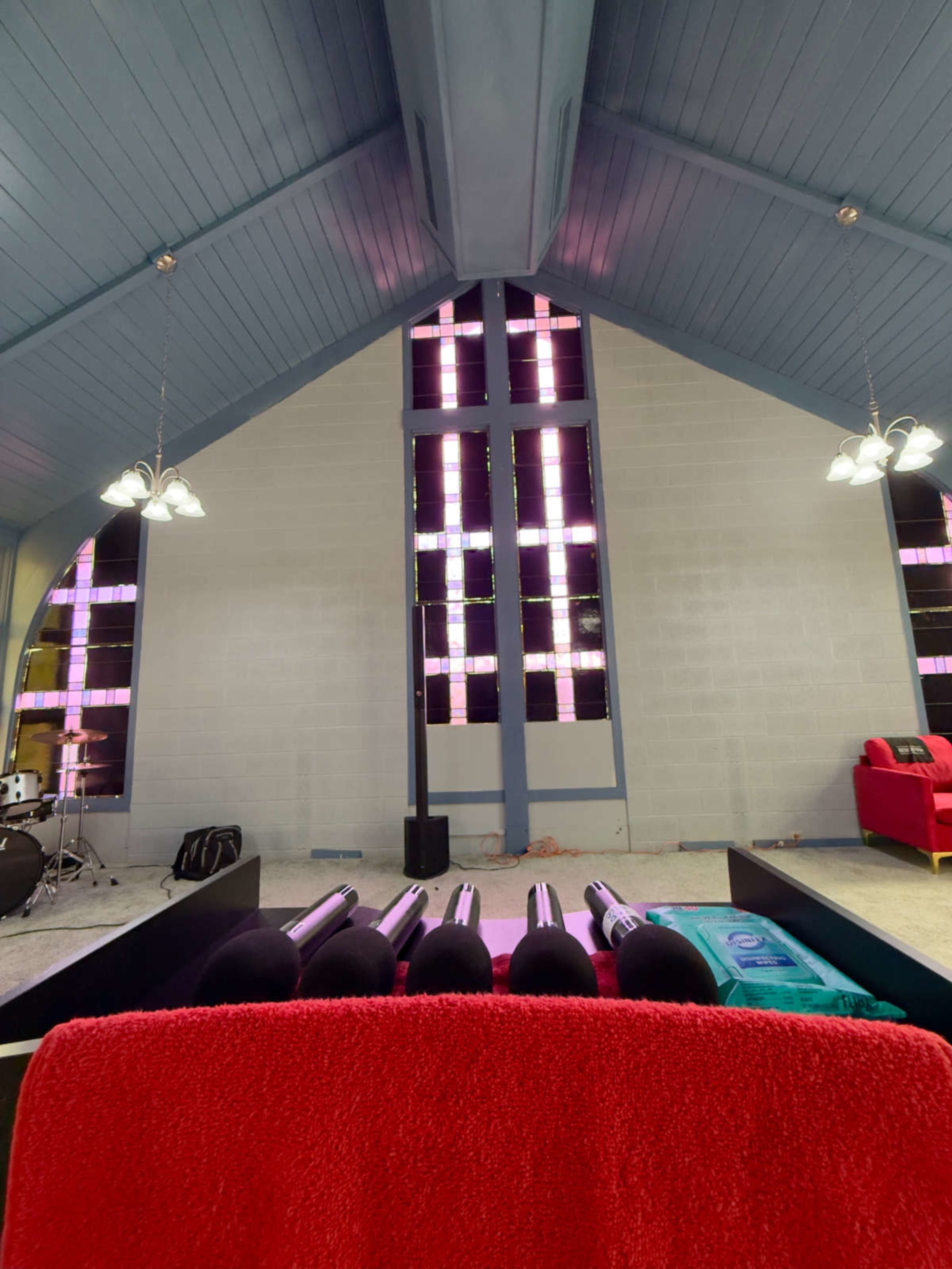 The image shows the interior of a modern church with colorful stained glass windows and a seating area featuring red and black furniture.
