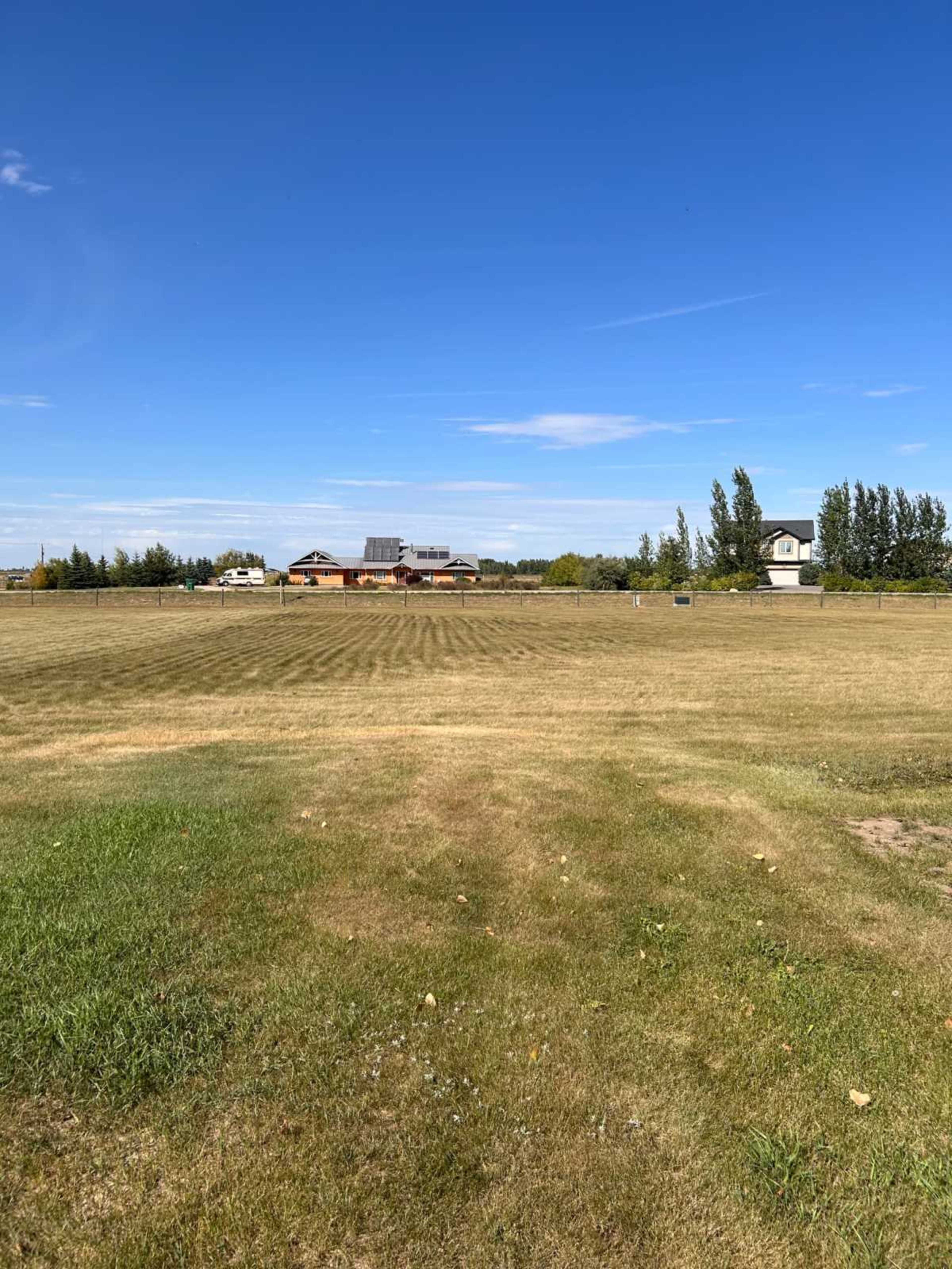A grassy field extends towards several buildings under a clear blue sky.