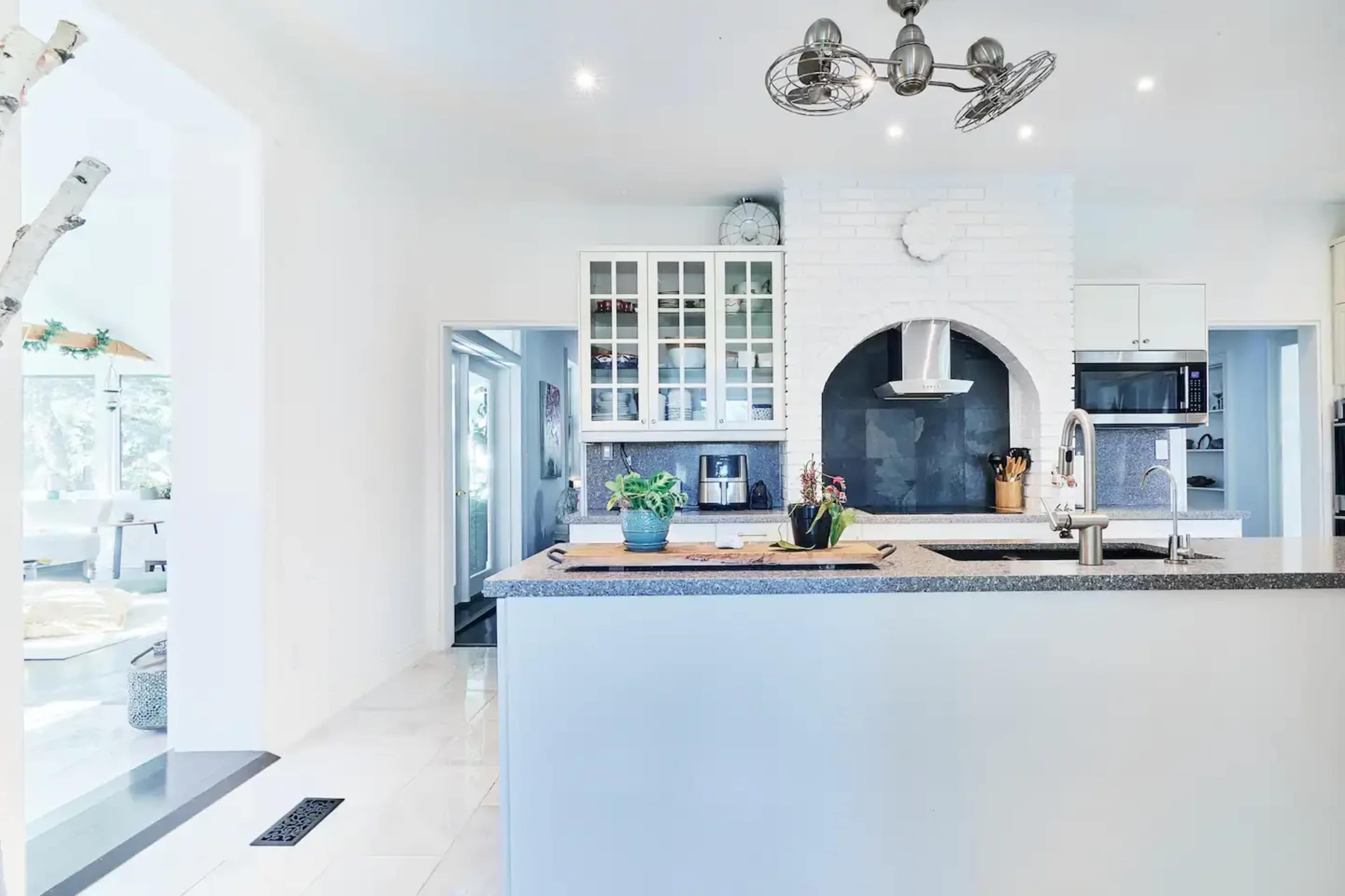 A modern kitchen with a central island, white cabinetry, and a slate grey countertop featuring a built-in stovetop and hood.