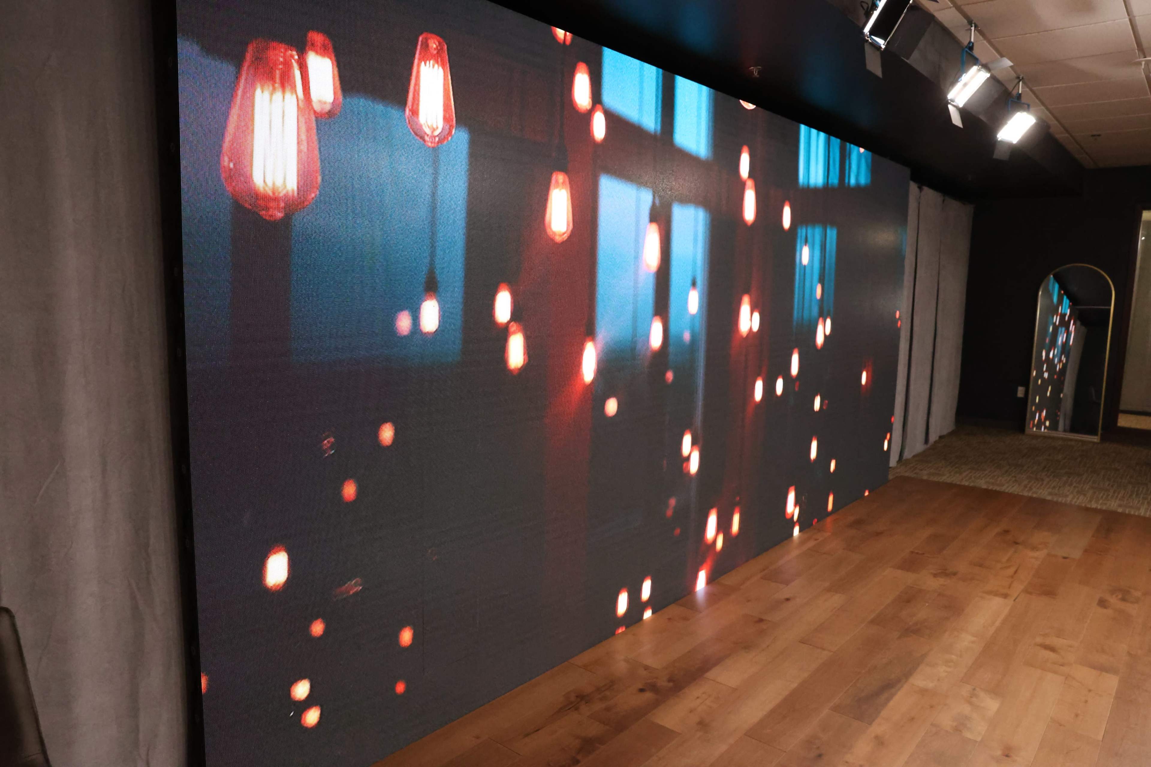 The image shows a large display wall featuring a digital design with illuminated pendant lights against a dark background.