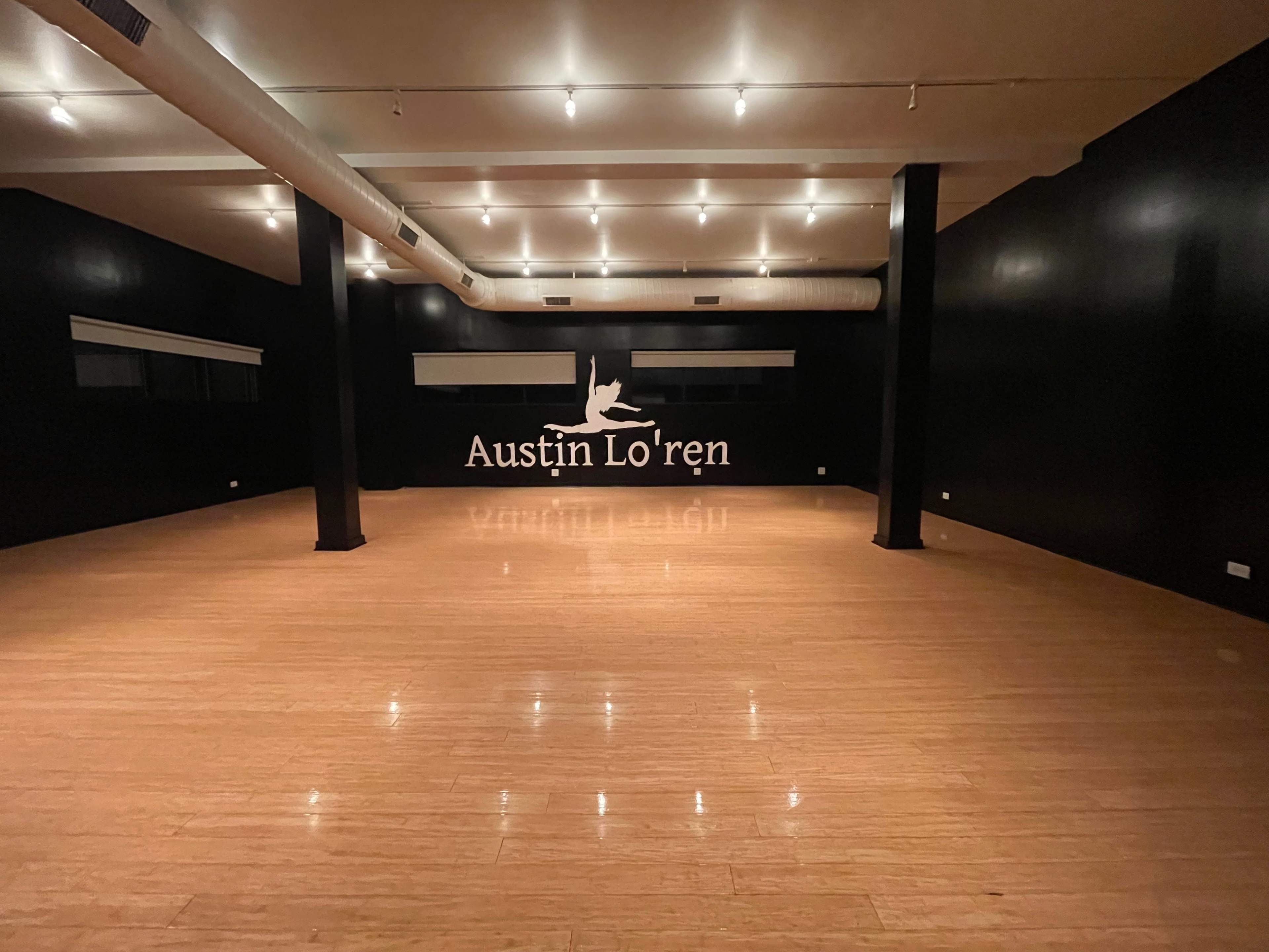 The image shows an empty dance studio with a wooden floor and a wall featuring the name "Austin Lo'ren" in large white letters.