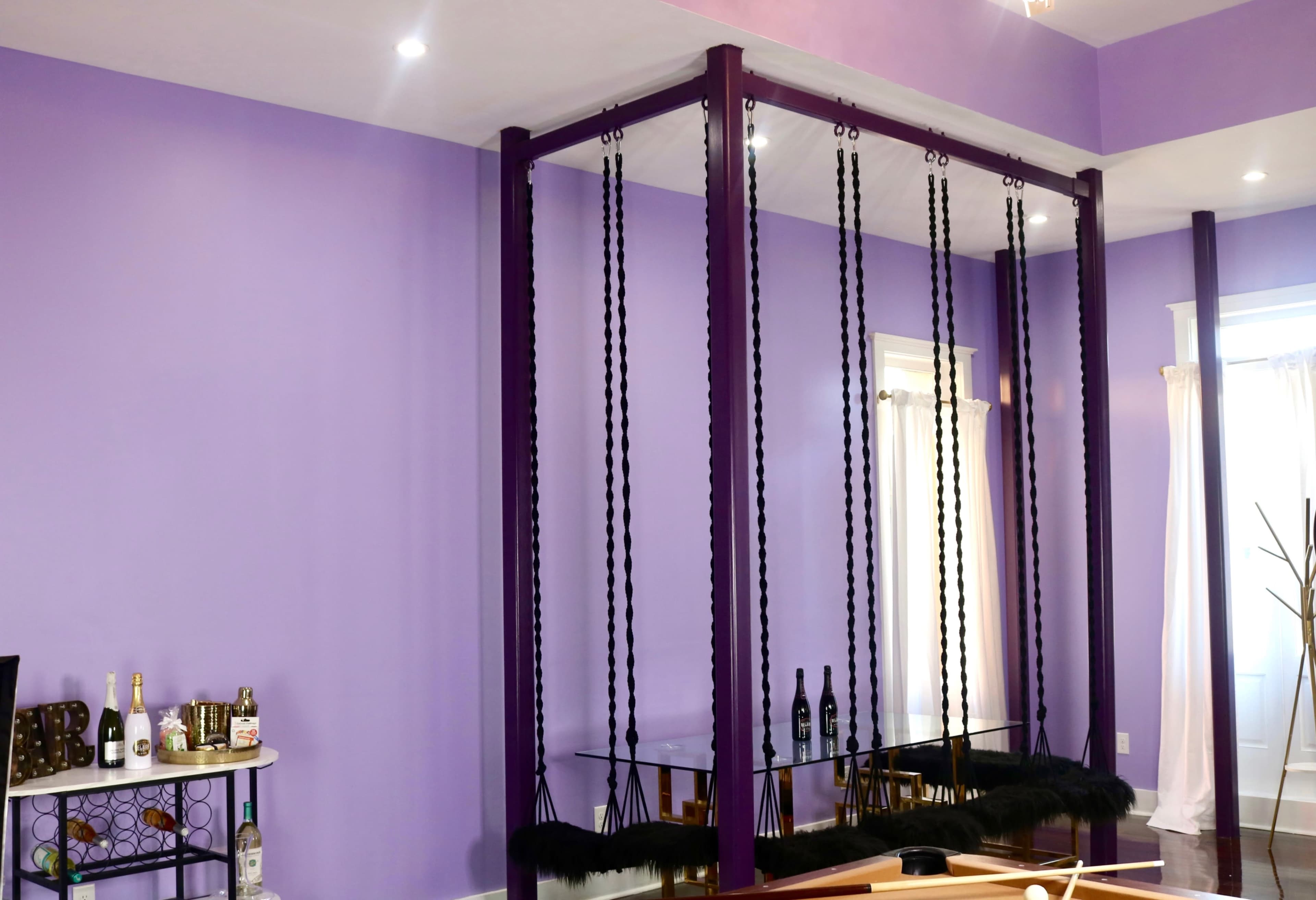 A room with purple walls featuring a large, purple framing structure with hanging ropes and a mirrored base.