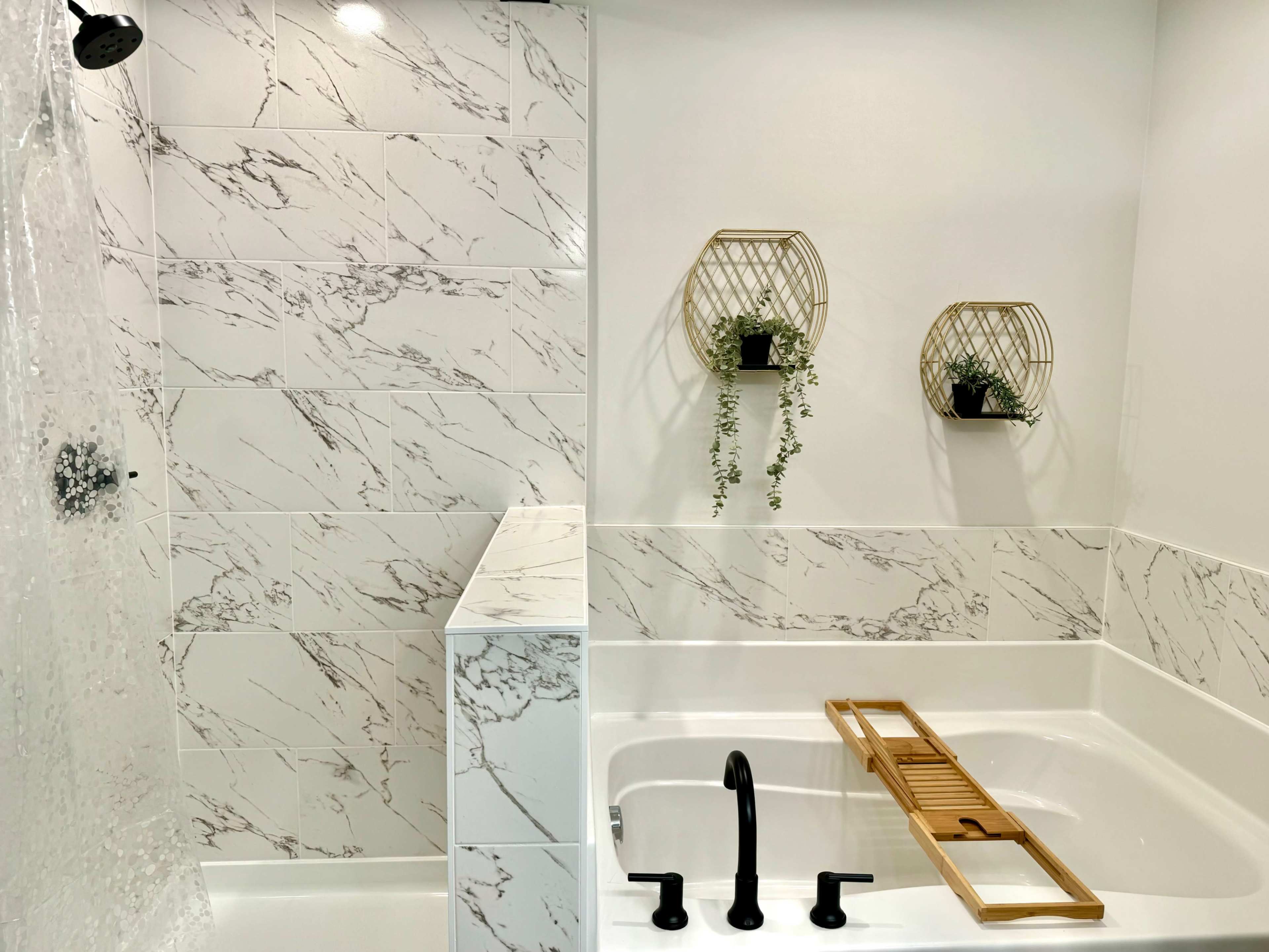 The bathroom features a shower with a glass door, a white bathtub with a wood bath tray, and decorative wall planters with greenery.