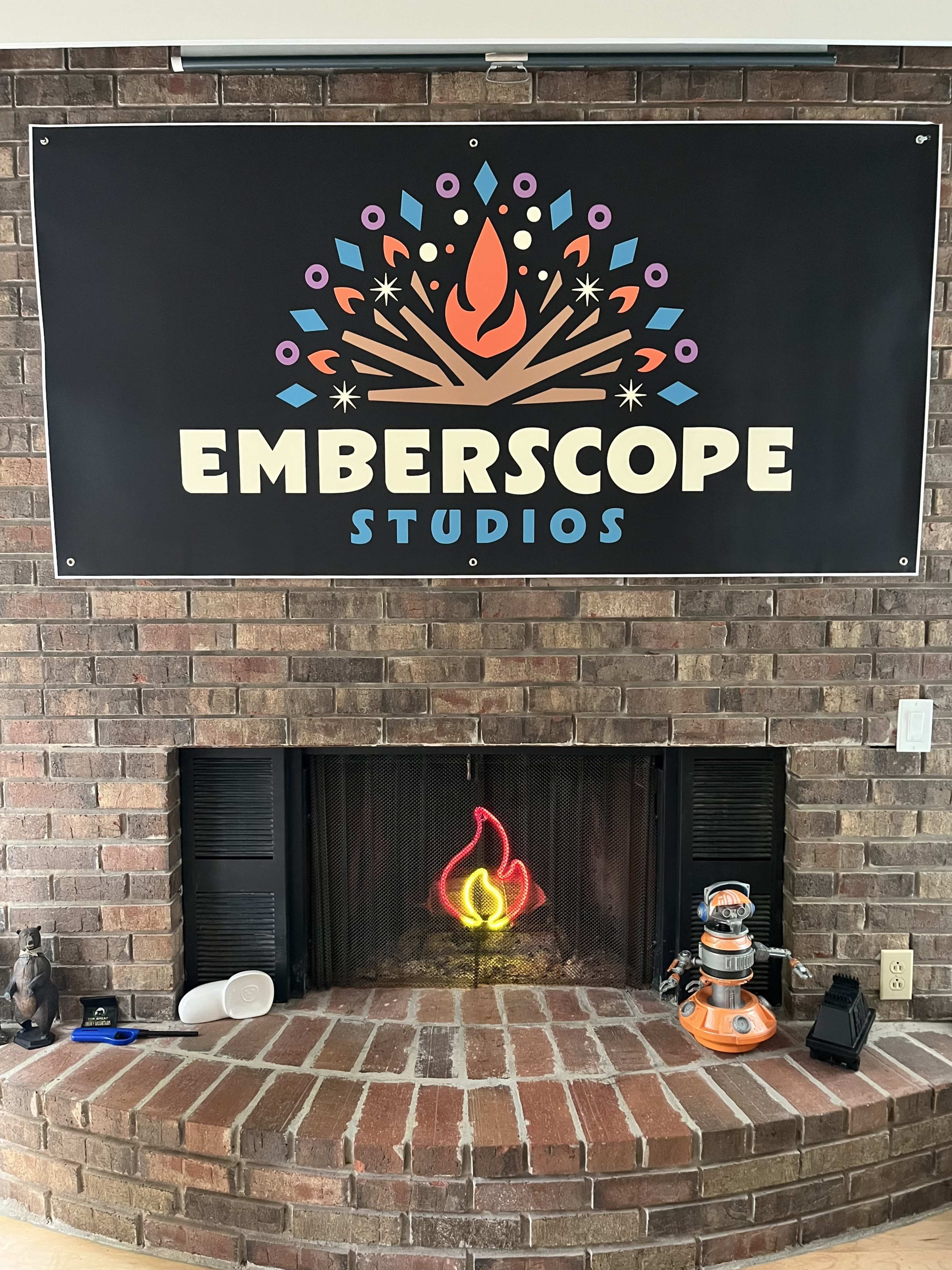 The image shows a brick fireplace with a colorful "Emberscope Studios" banner above it, featuring a stylized flame design.