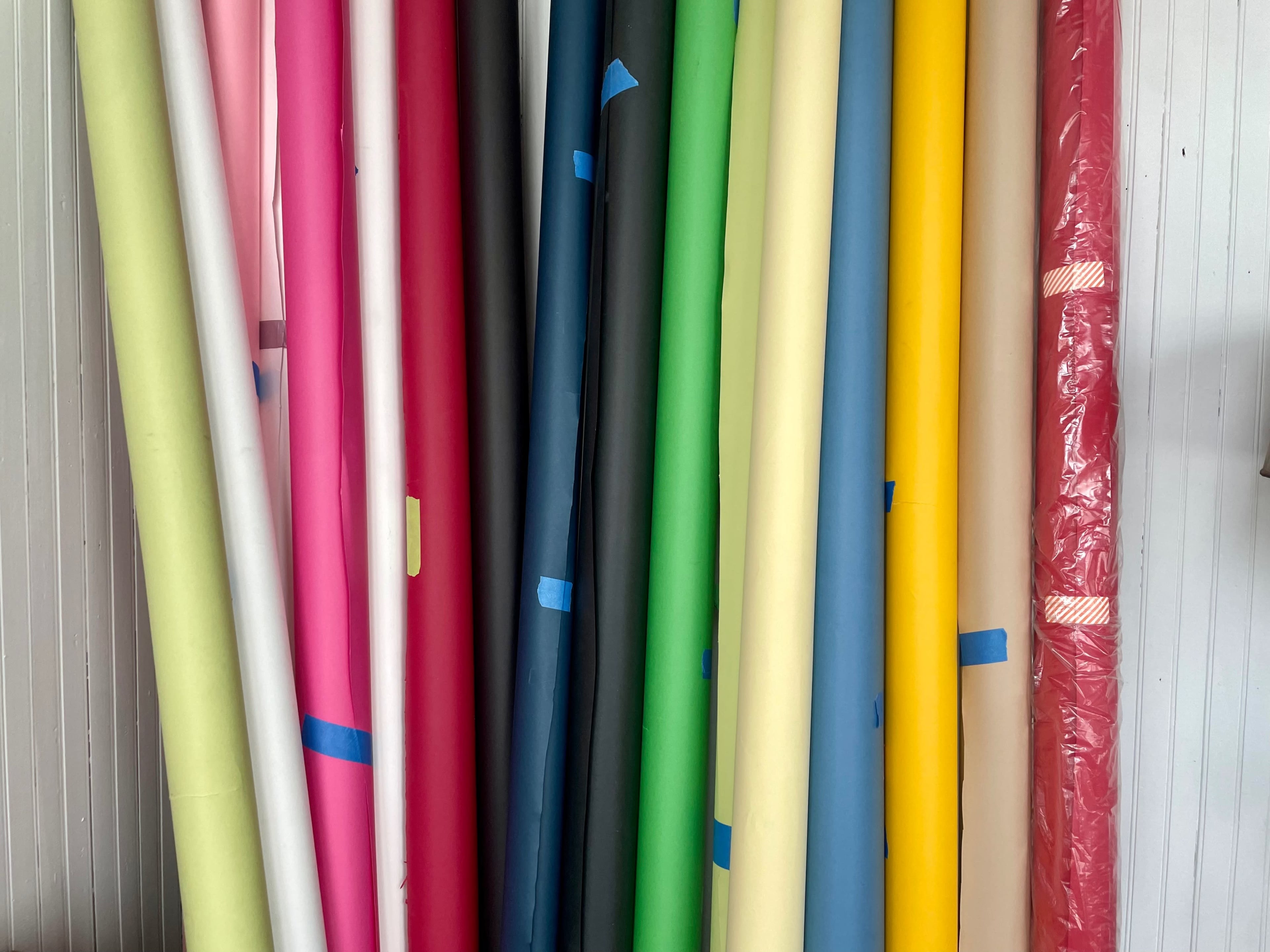 A collection of rolled paper in various colors stacked against a wall.