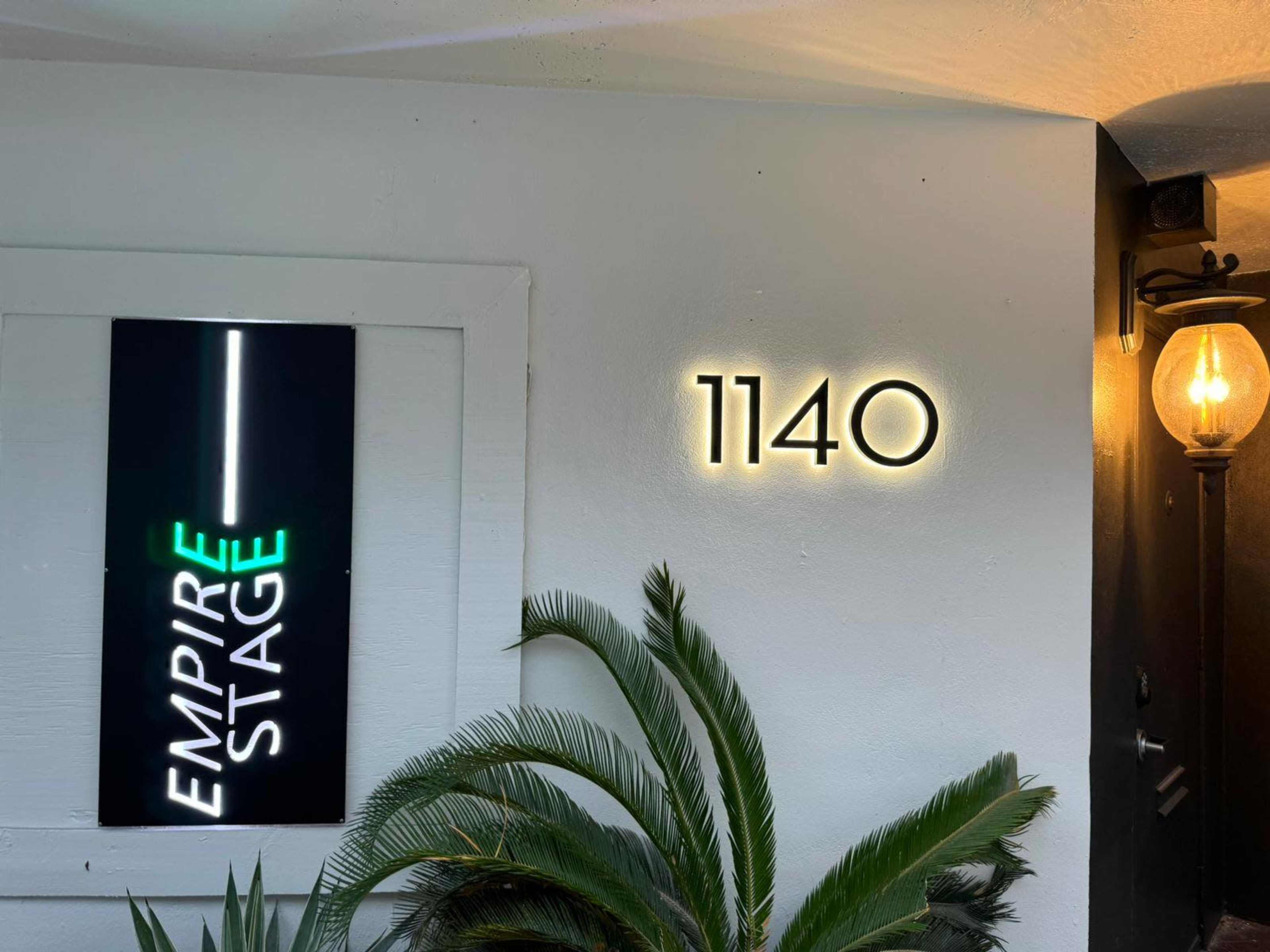 The image shows a wall with a lighted sign reading "EMPIRE STAGE" and a separate illuminated number "1140" next to a lamp and a green plant.