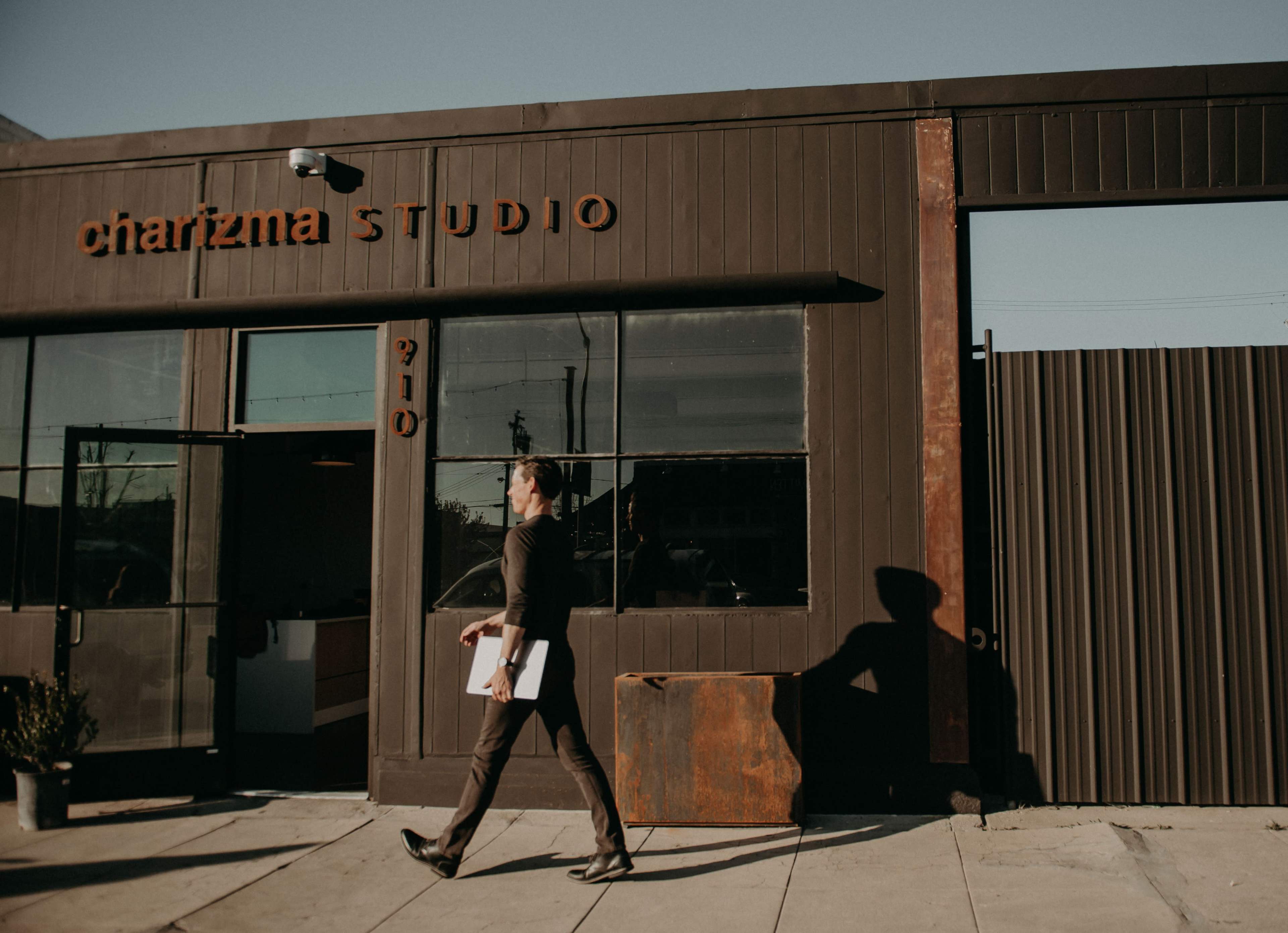 A man walks past a building with a sign reading "charizma STUDIO" on the exterior.