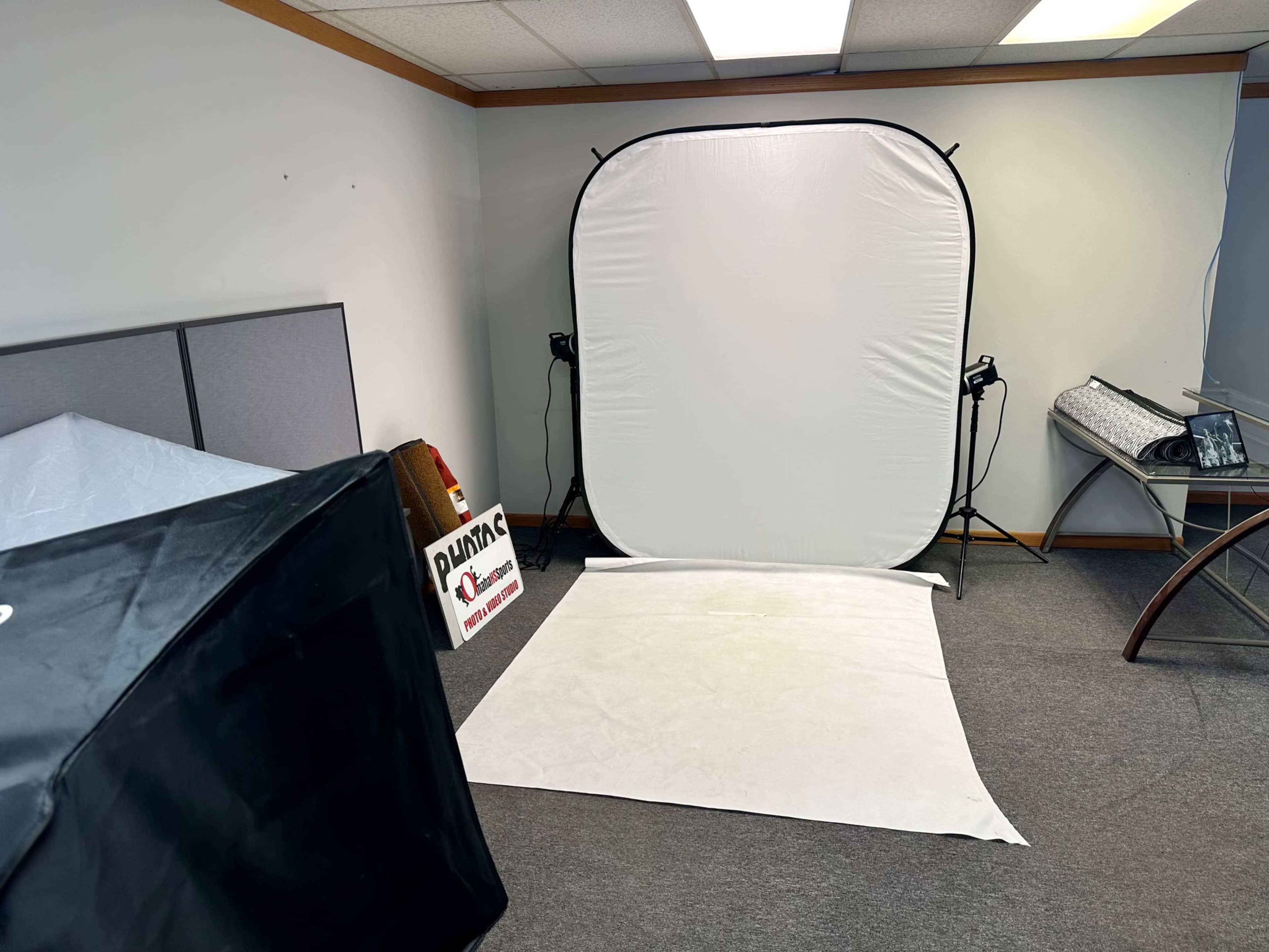 The image shows a room with a plain white backdrop setup for photography, along with a black tent and various equipment.