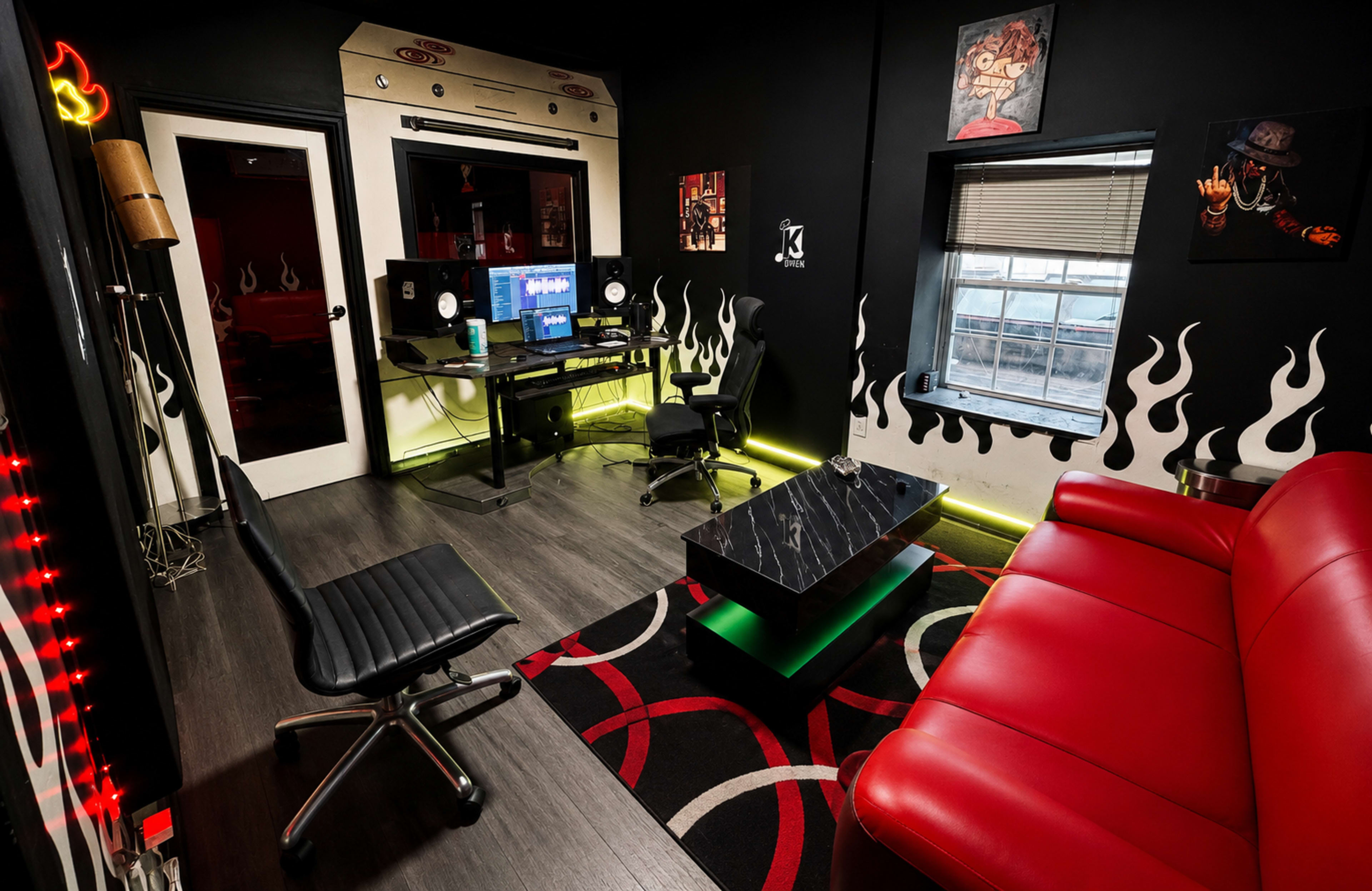 The image shows a modern studio room featuring a black and red color scheme, equipped with a desk holding audio equipment, a red sofa, and decorative flame motifs on the walls.