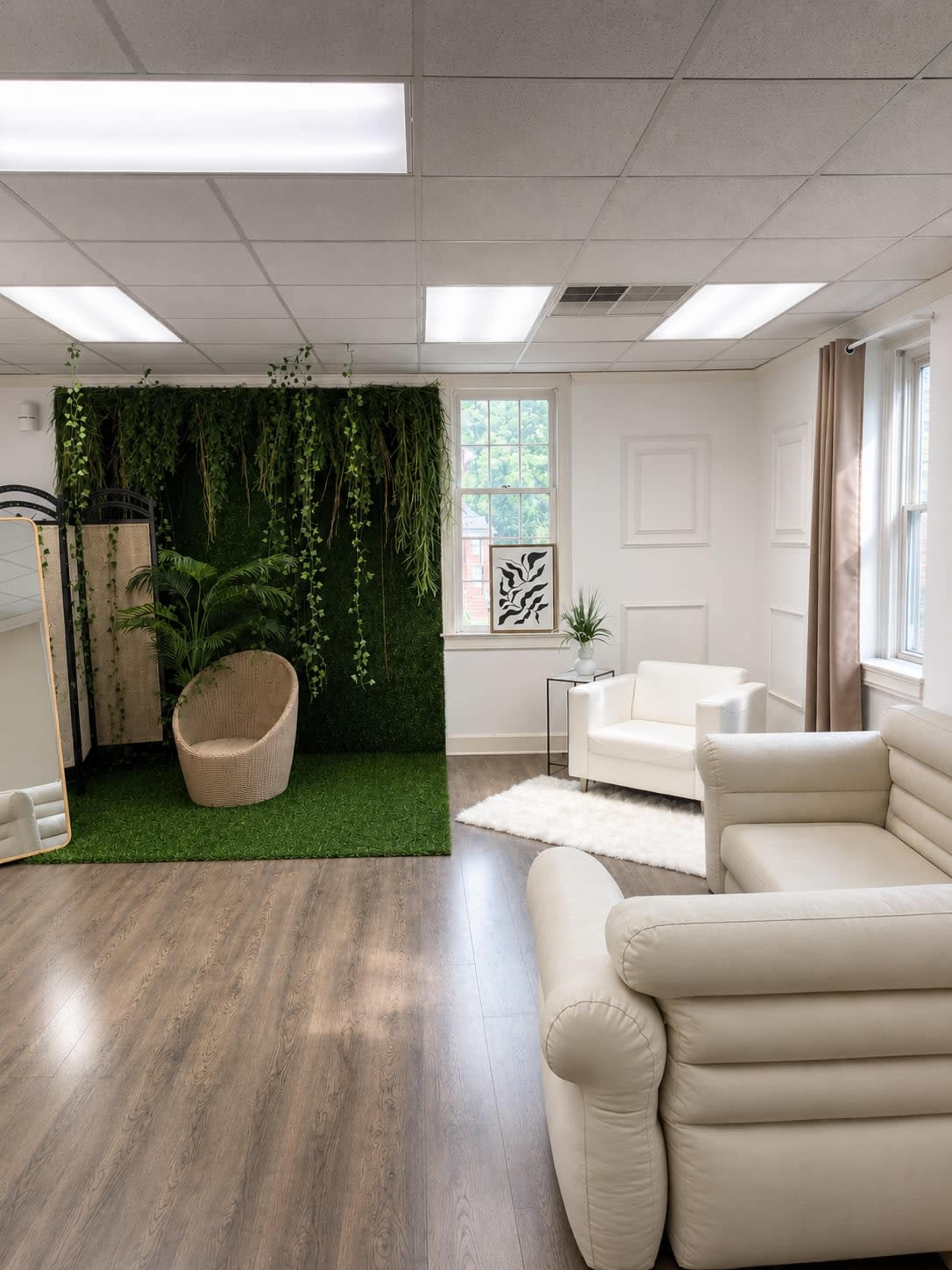 The image shows a modern office space featuring a green vertical garden, a round chair, a white sofa, and large windows allowing natural light.