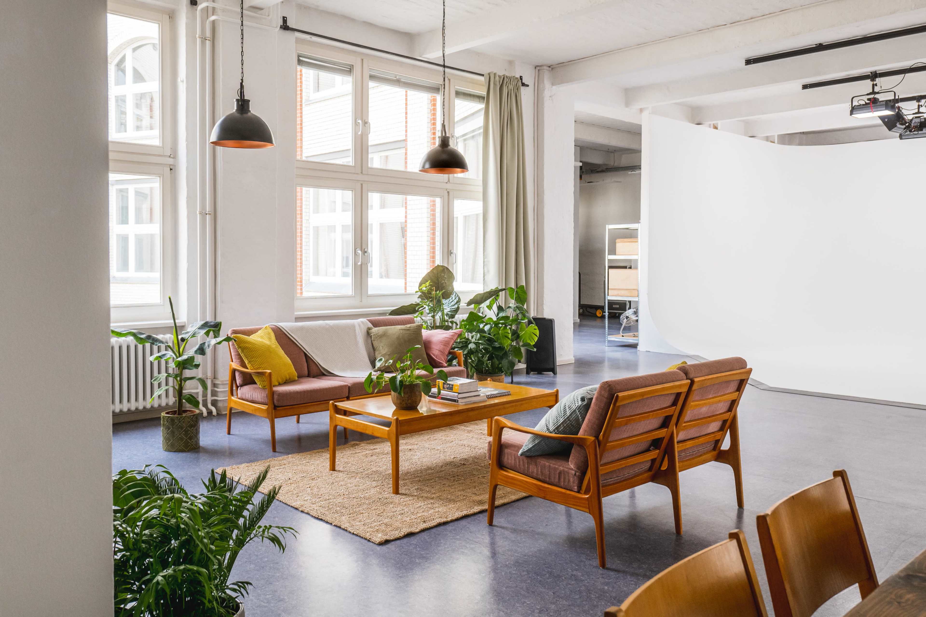 A modern lounge area features wooden furniture, potted plants, and large windows allowing natural light to fill the space.