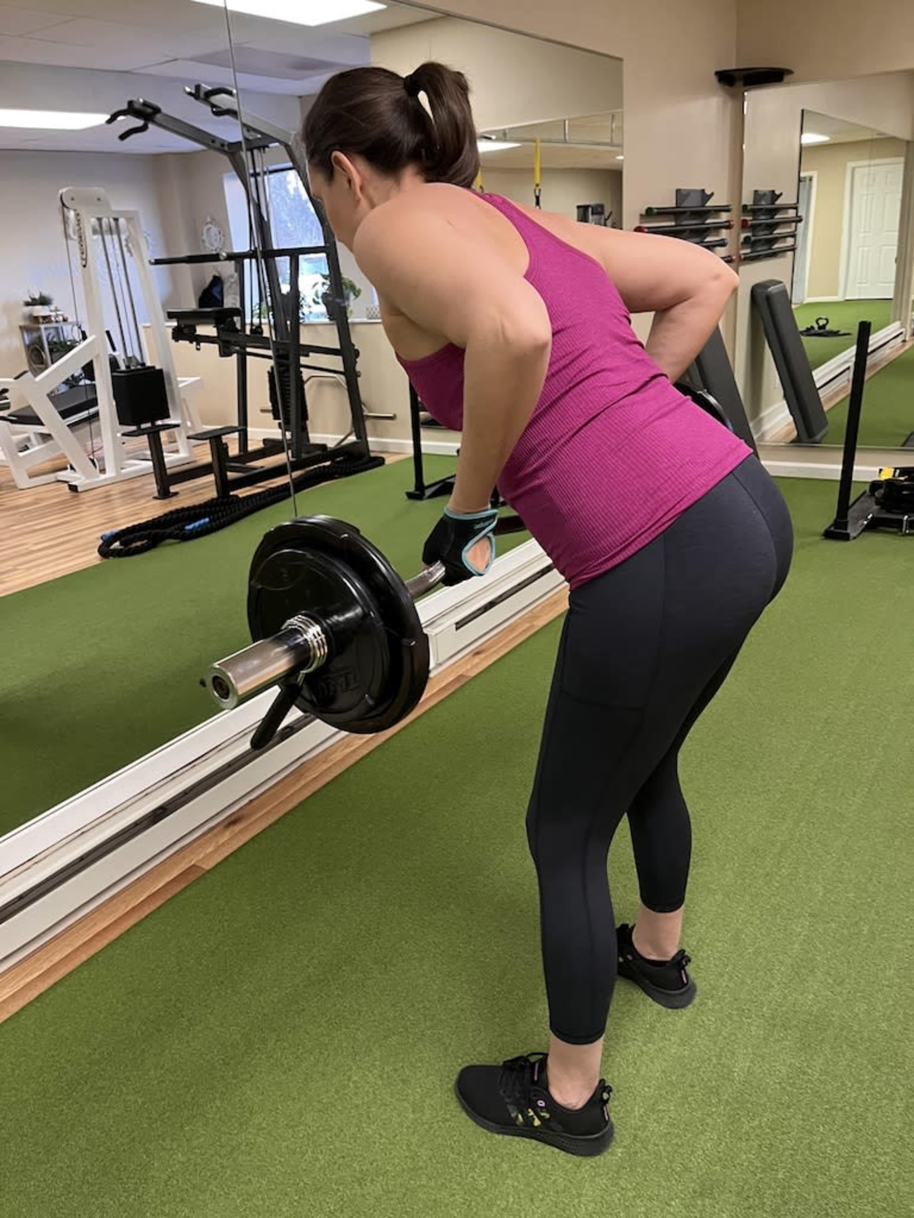 A woman performs a bent-over row exercise with a barbell in a gym setting.
