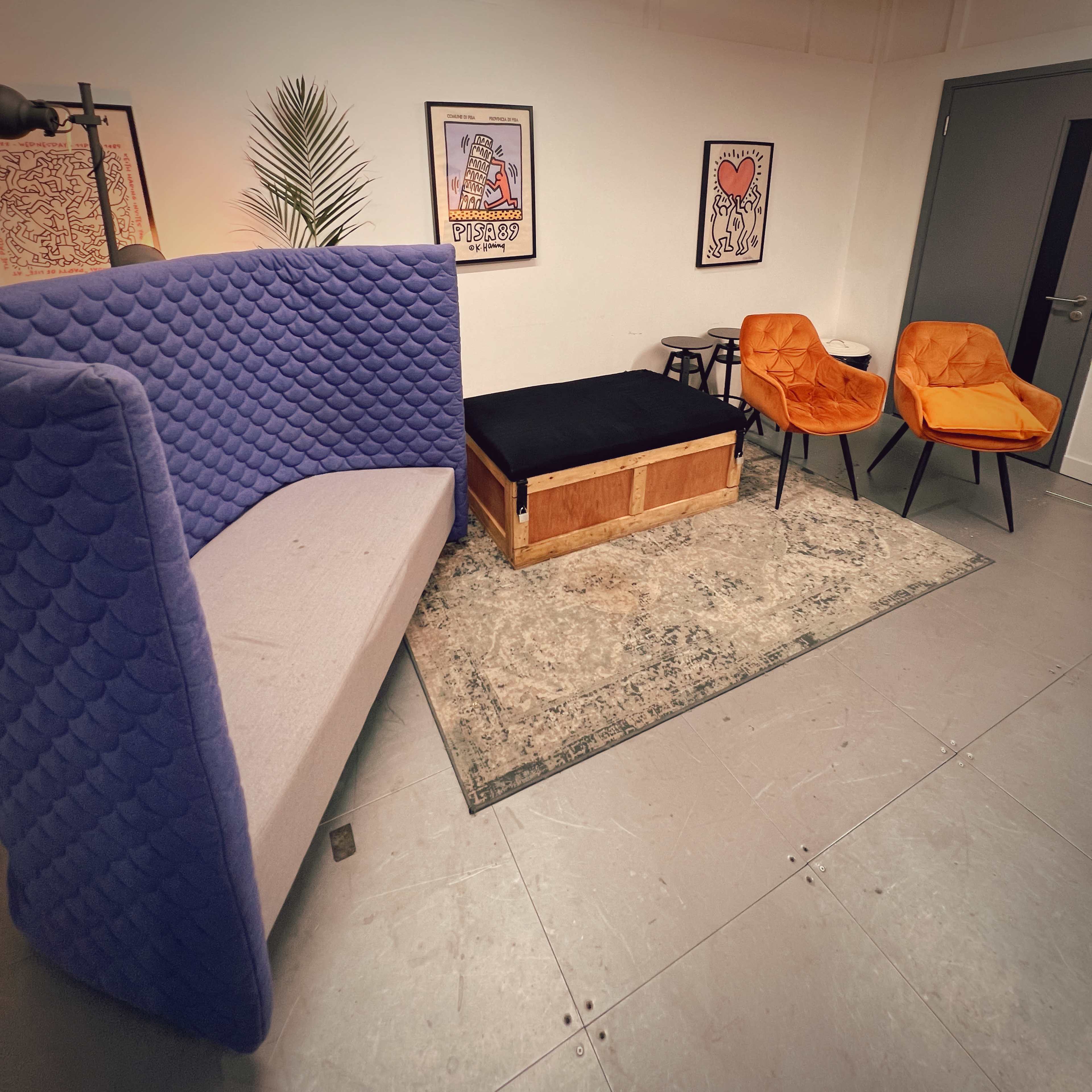 A modern room with a purple fabric sofa, two orange chairs, a low wooden table, and a decorative rug on the floor.