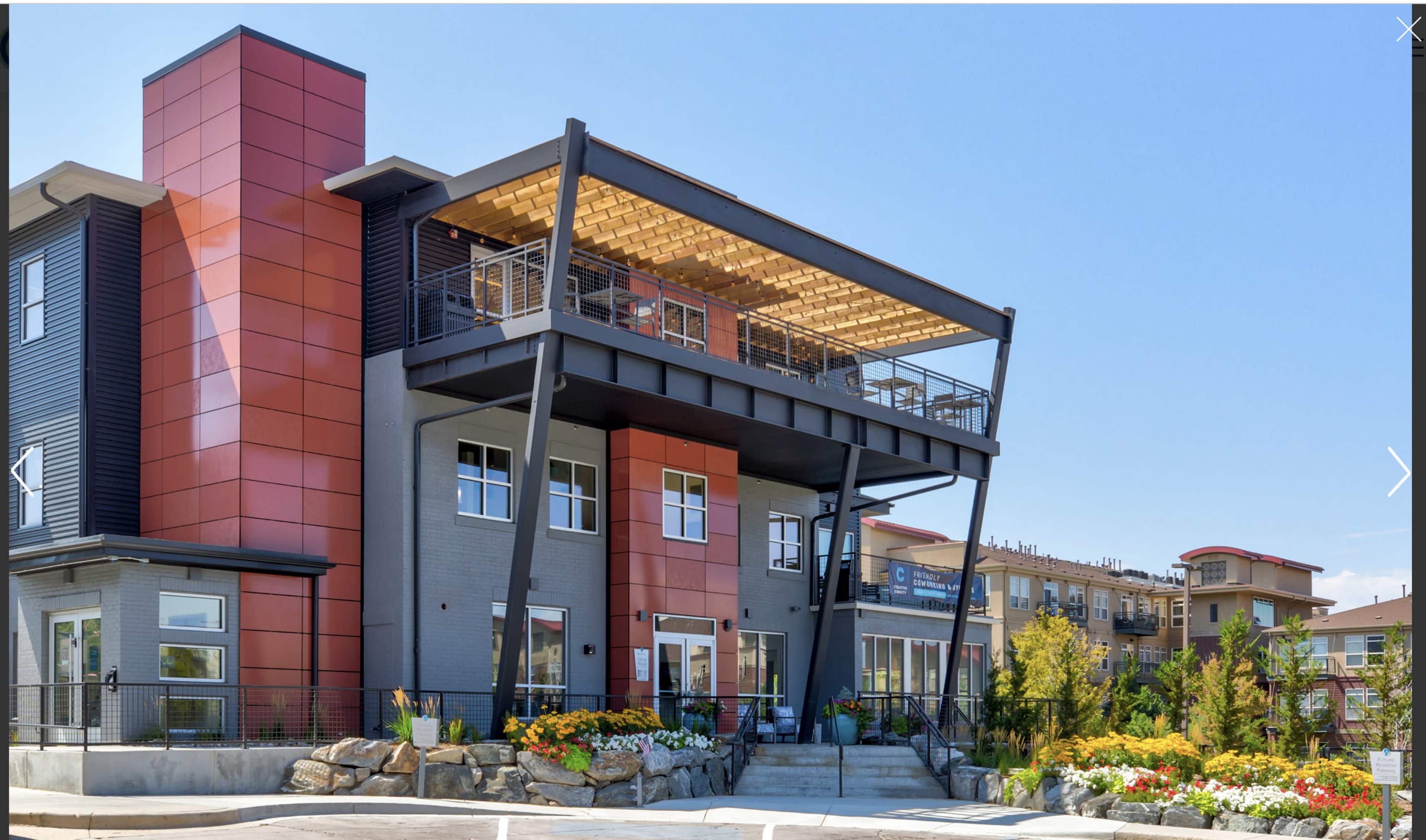 A contemporary multi-story building with a covered balcony and colorful landscaping in front.