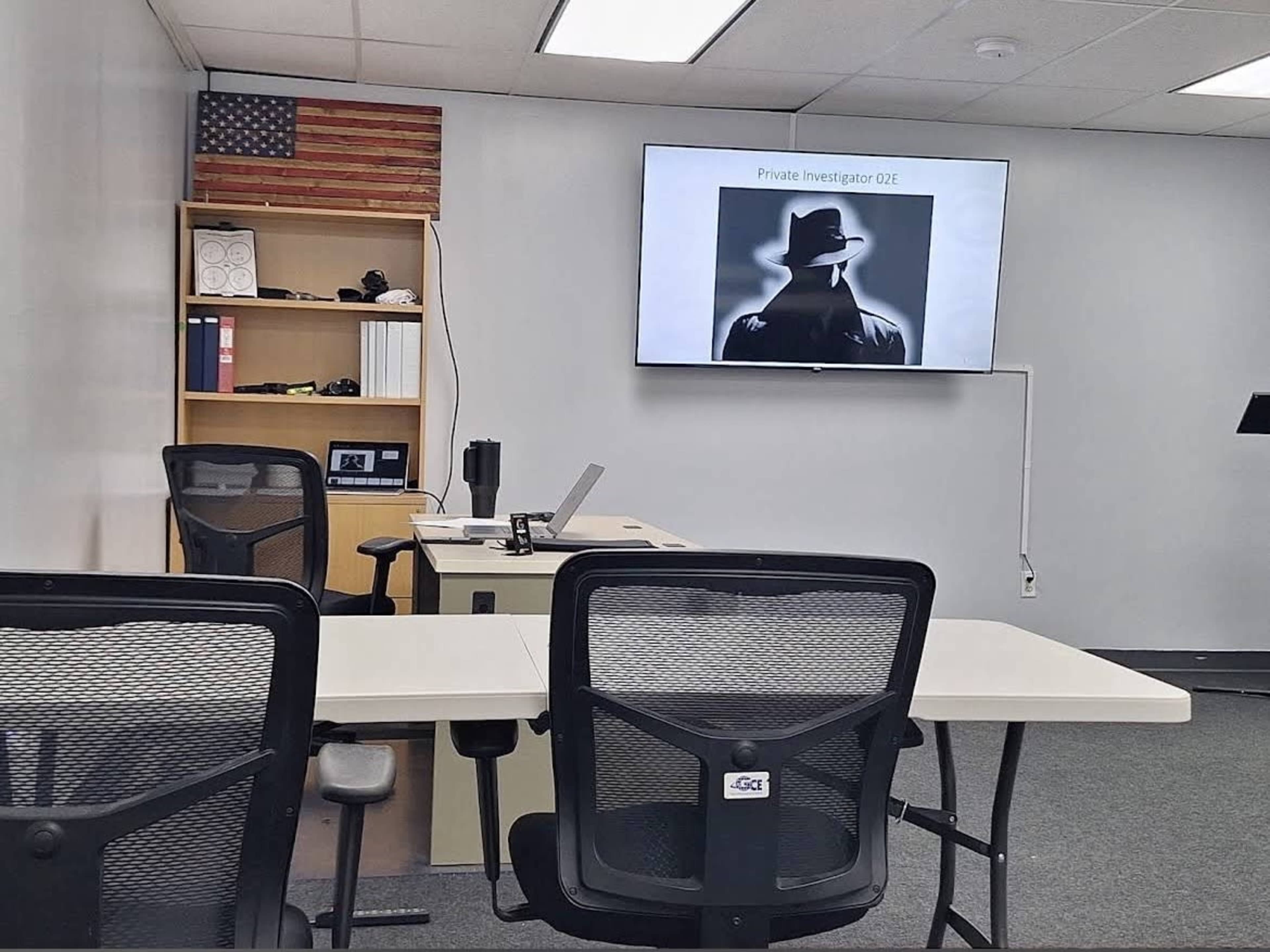 The image shows a modern conference room with a presentation screen displaying "Private Investigator 02E," a desk with notebooks, and several empty chairs arranged around the table.