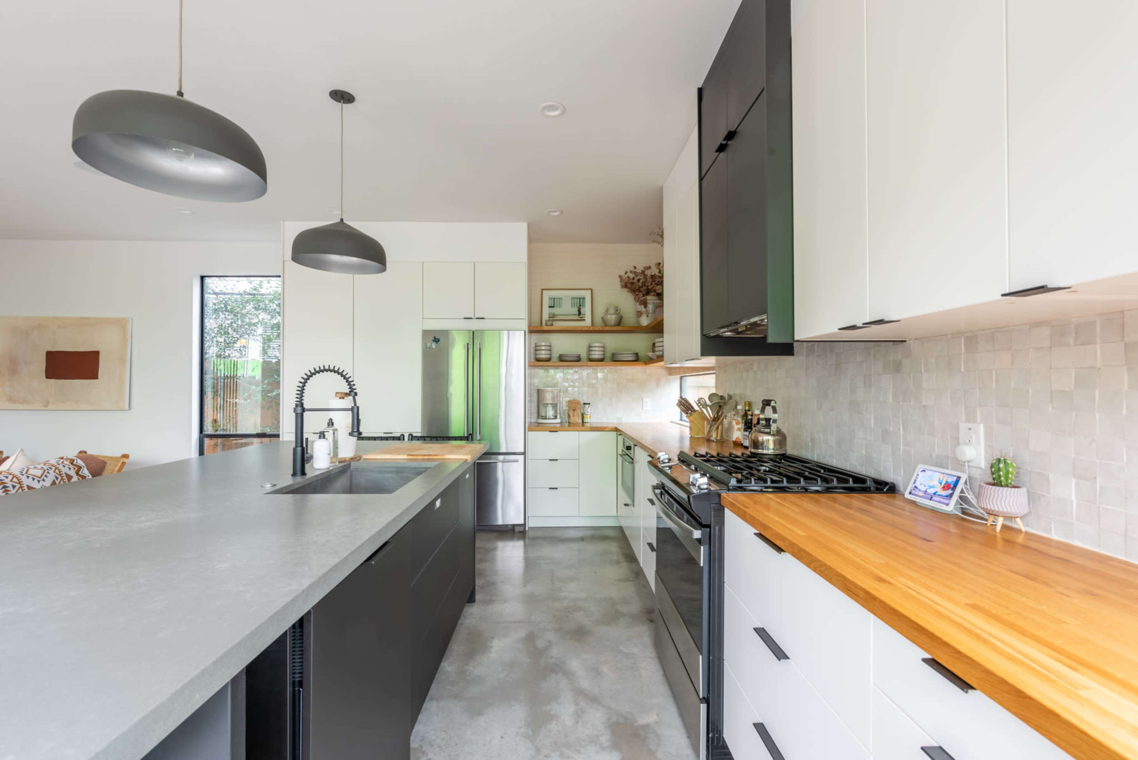 The kitchen features a central island with a concrete countertop, black and white cabinetry, and stainless steel appliances.