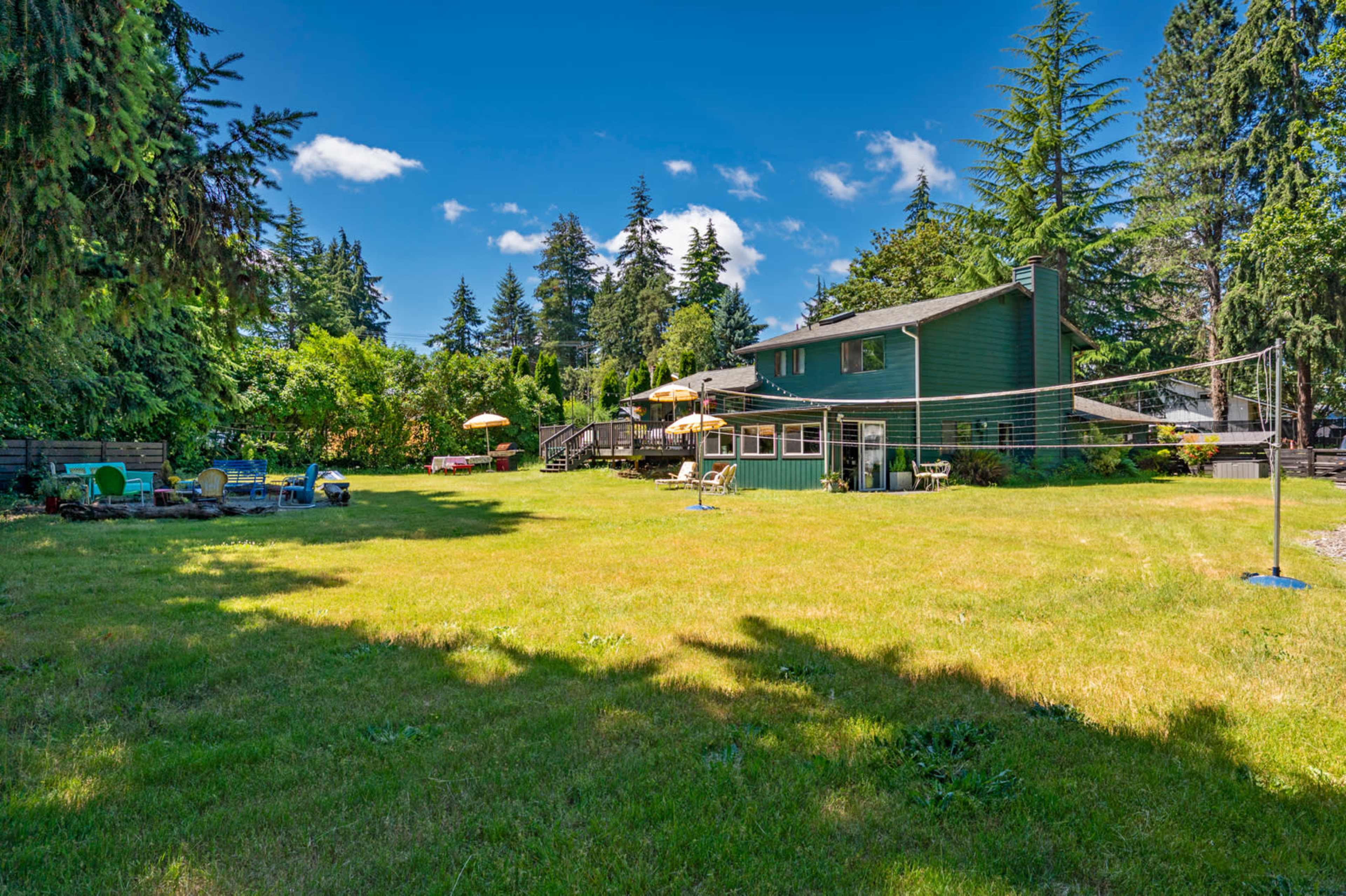 A spacious backyard features a green lawn, a house in the background, and a volleyball net set up.