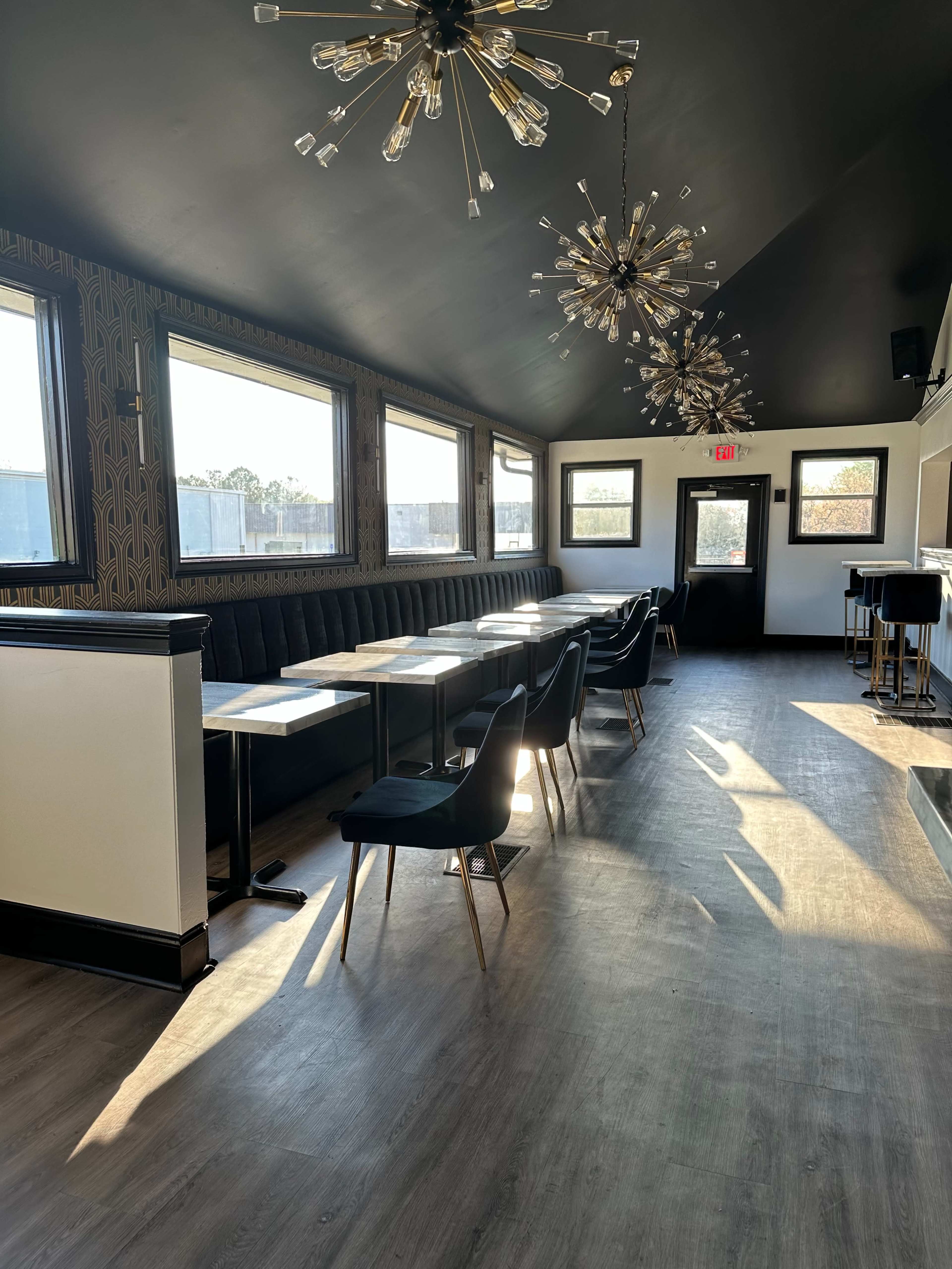 The image shows a modern restaurant interior with rows of seating, large windows letting in natural light, and decorative light fixtures hanging from the ceiling.