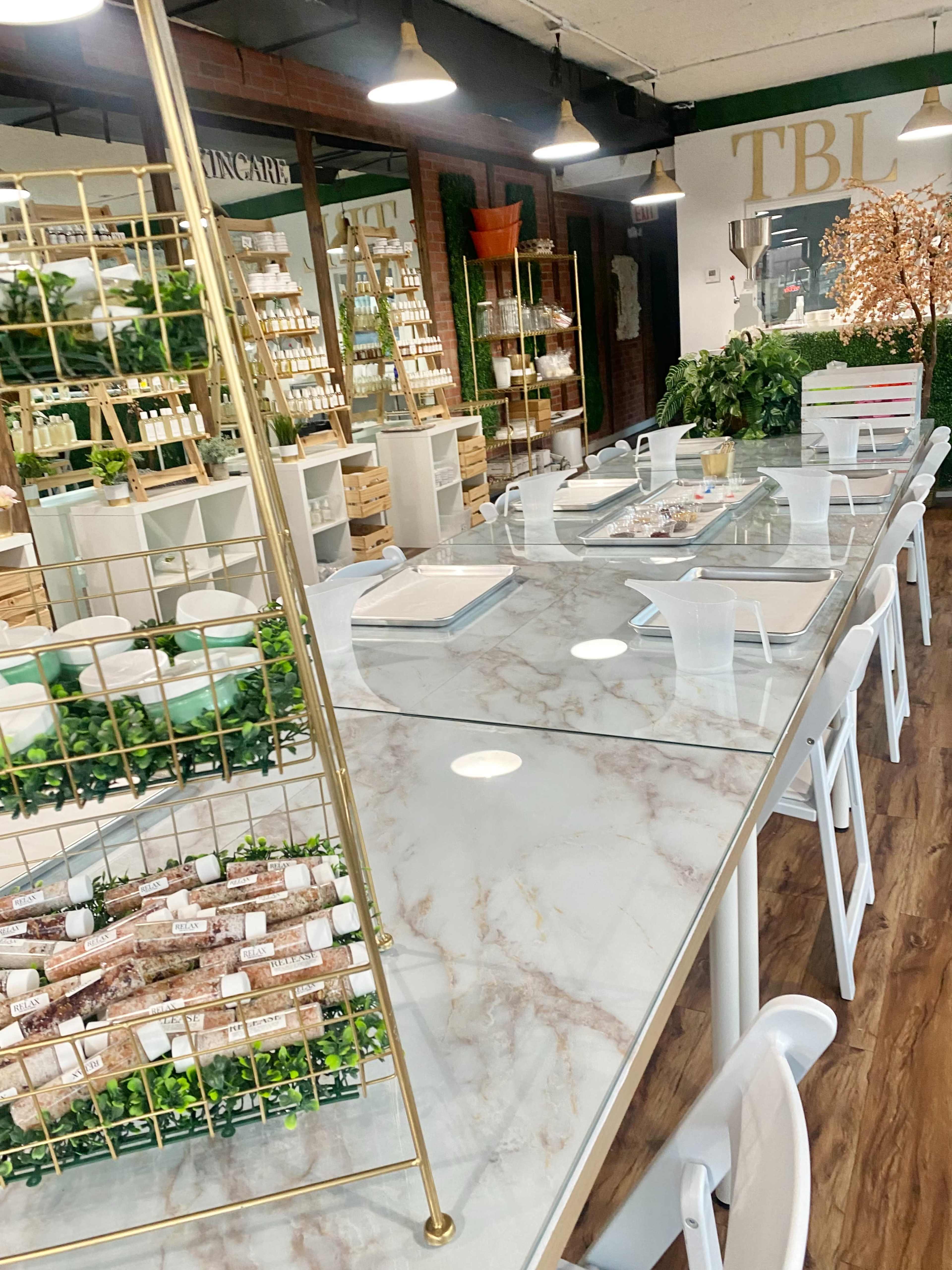 A modern retail space with a marble table surrounded by white chairs, featuring shelves of skincare products and decorative greenery.