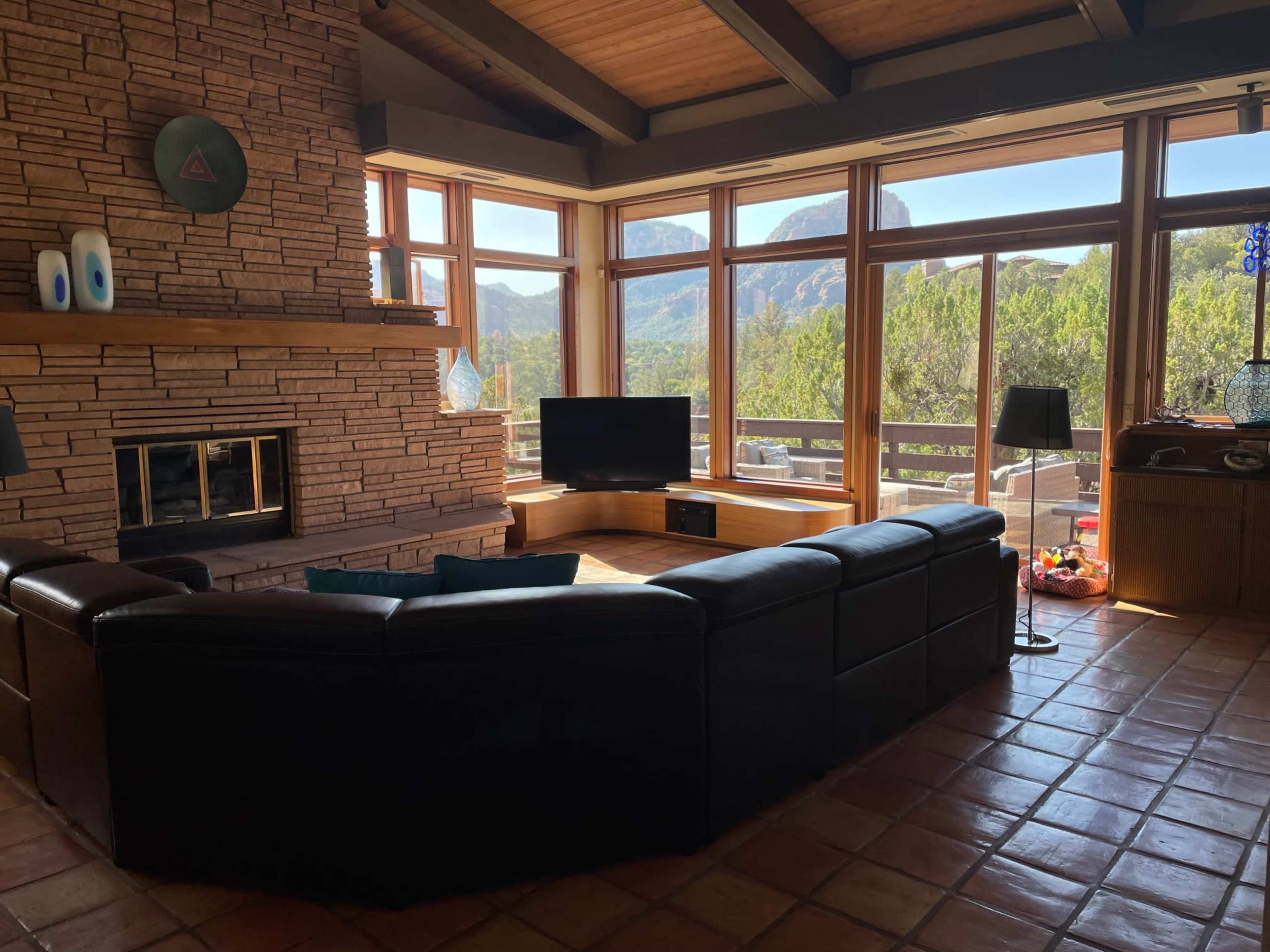 A spacious living room features large windows with mountain views, a stone fireplace, a sectional sofa, and a television.