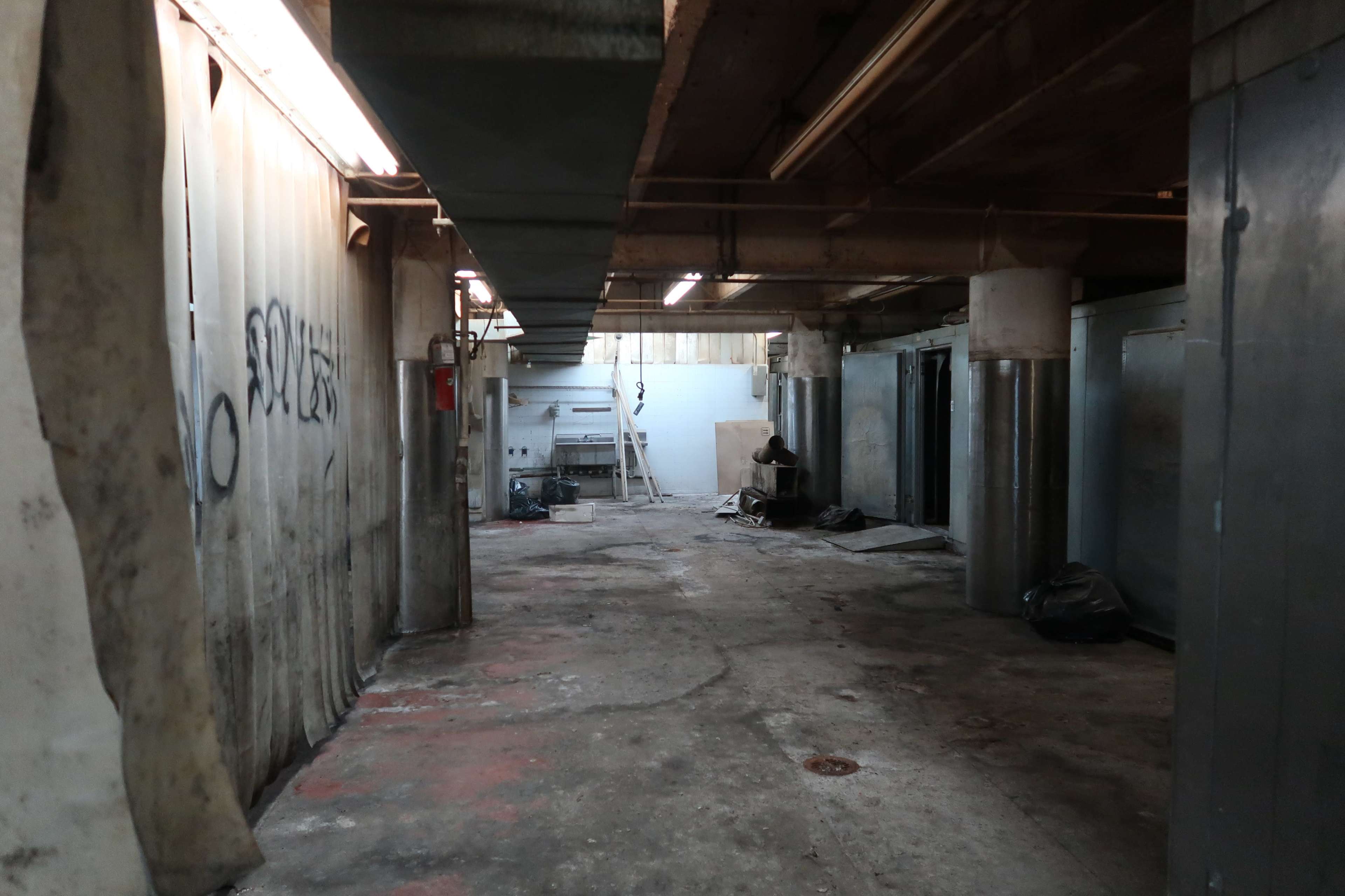 The image shows a dimly lit concrete corridor with partially visible storage units and scattered debris.