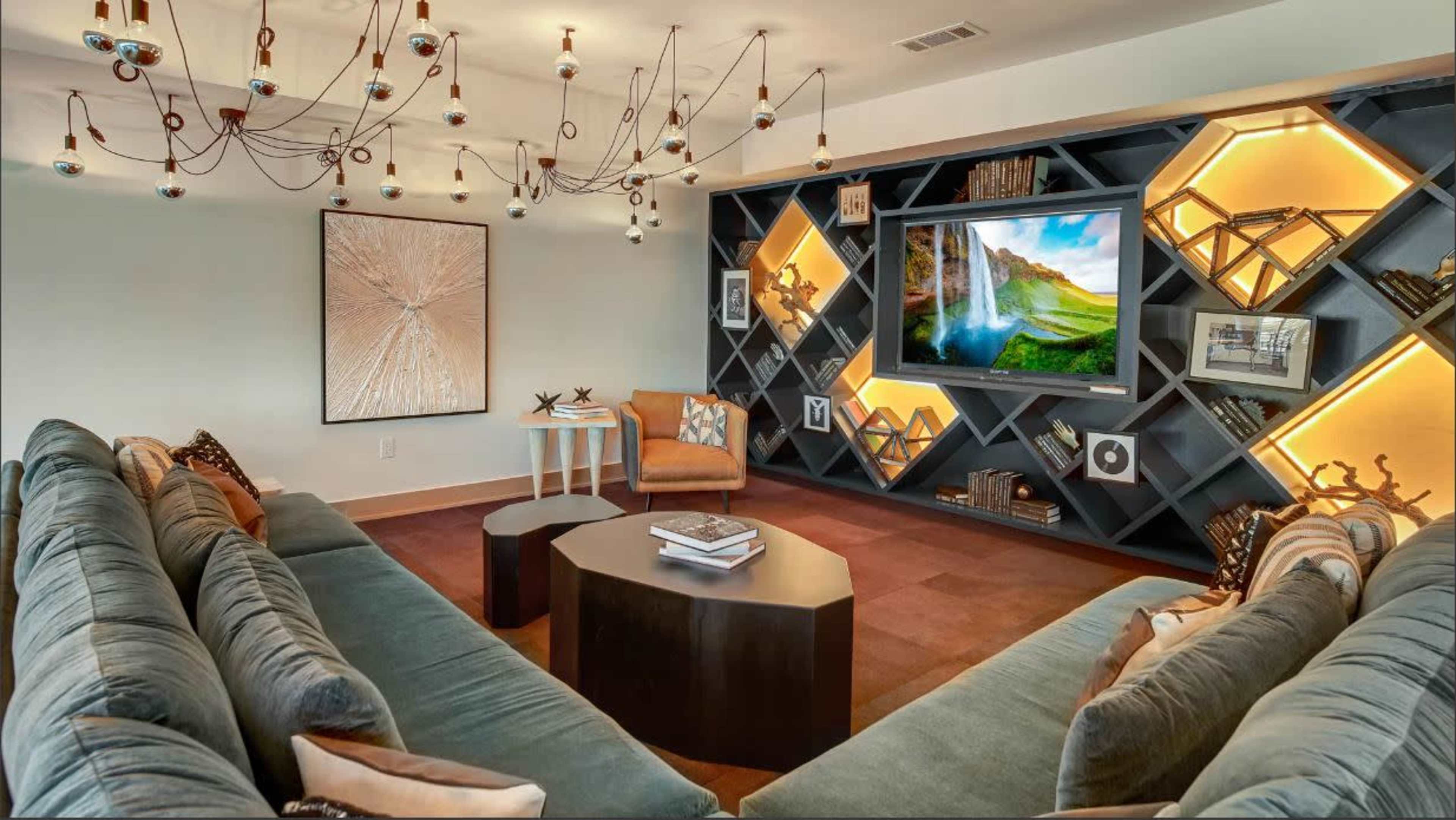 A modern living room featuring a sectional sofa, a coffee table, and a wall-mounted television set against a geometric bookshelf with decorative lighting.