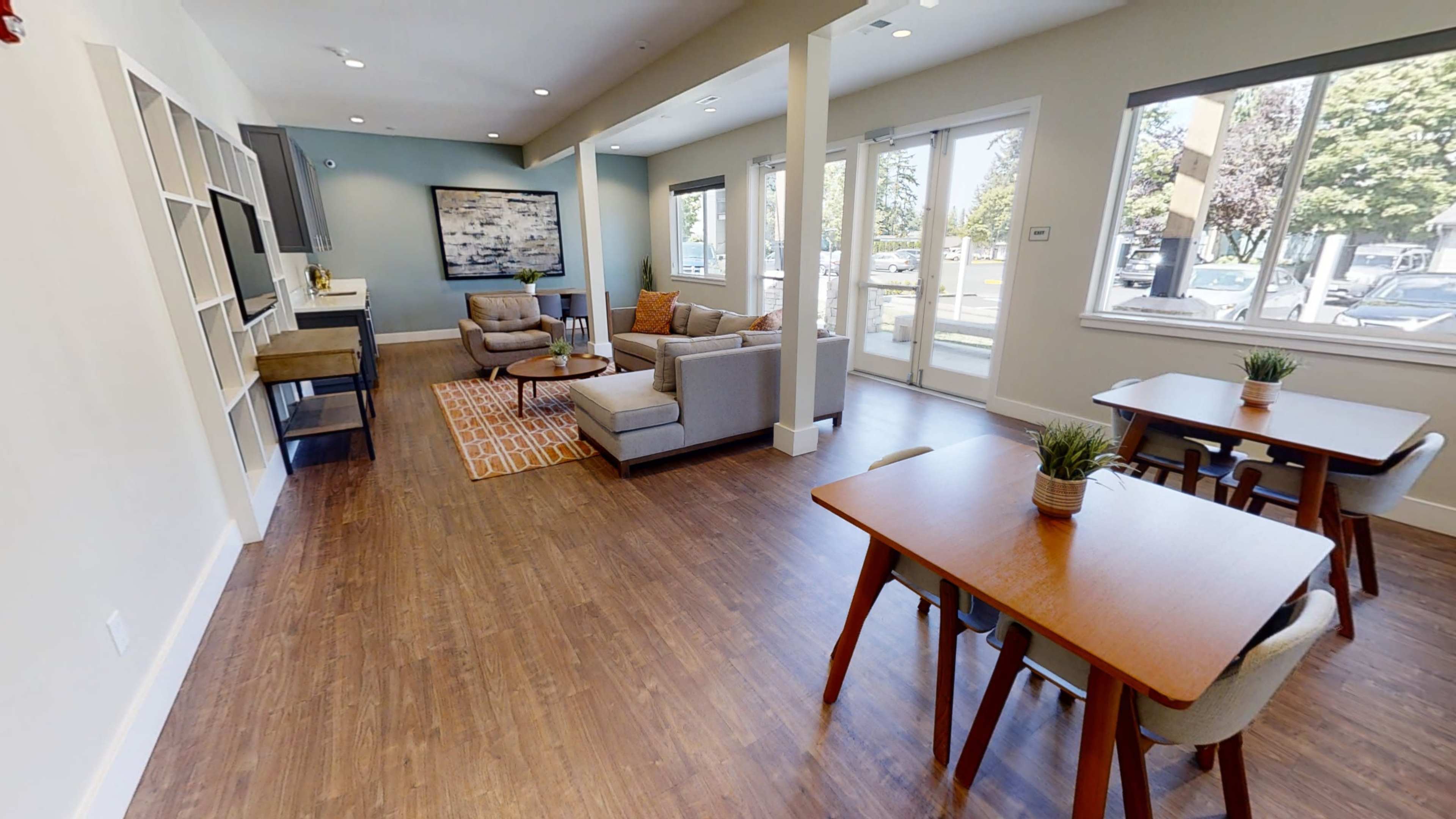 A modern common area with two tables, a seating arrangement, and large windows allowing natural light.