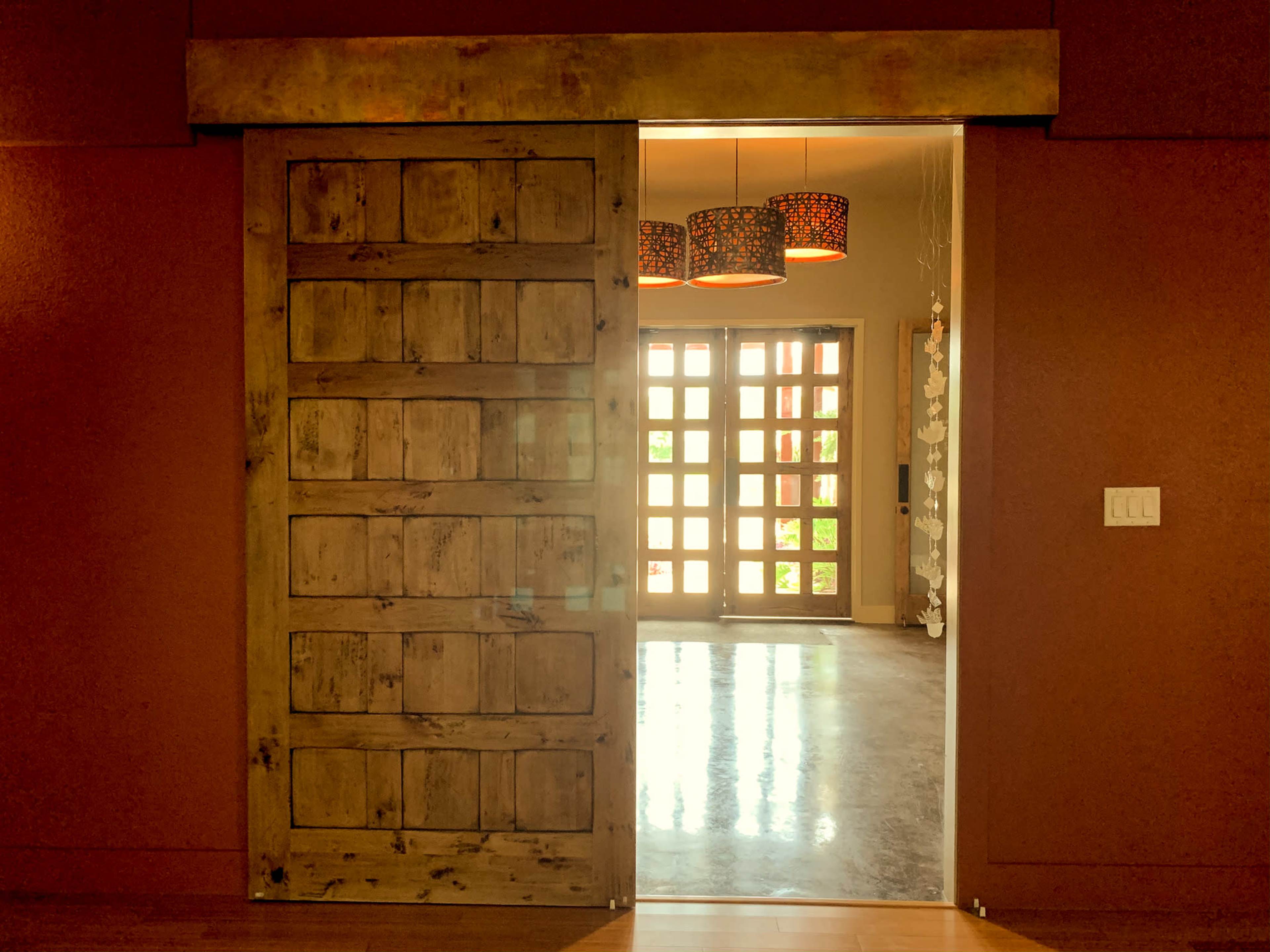 A wooden sliding door is partially open, revealing a brightly lit interior space with patterned light fixtures and large windows.