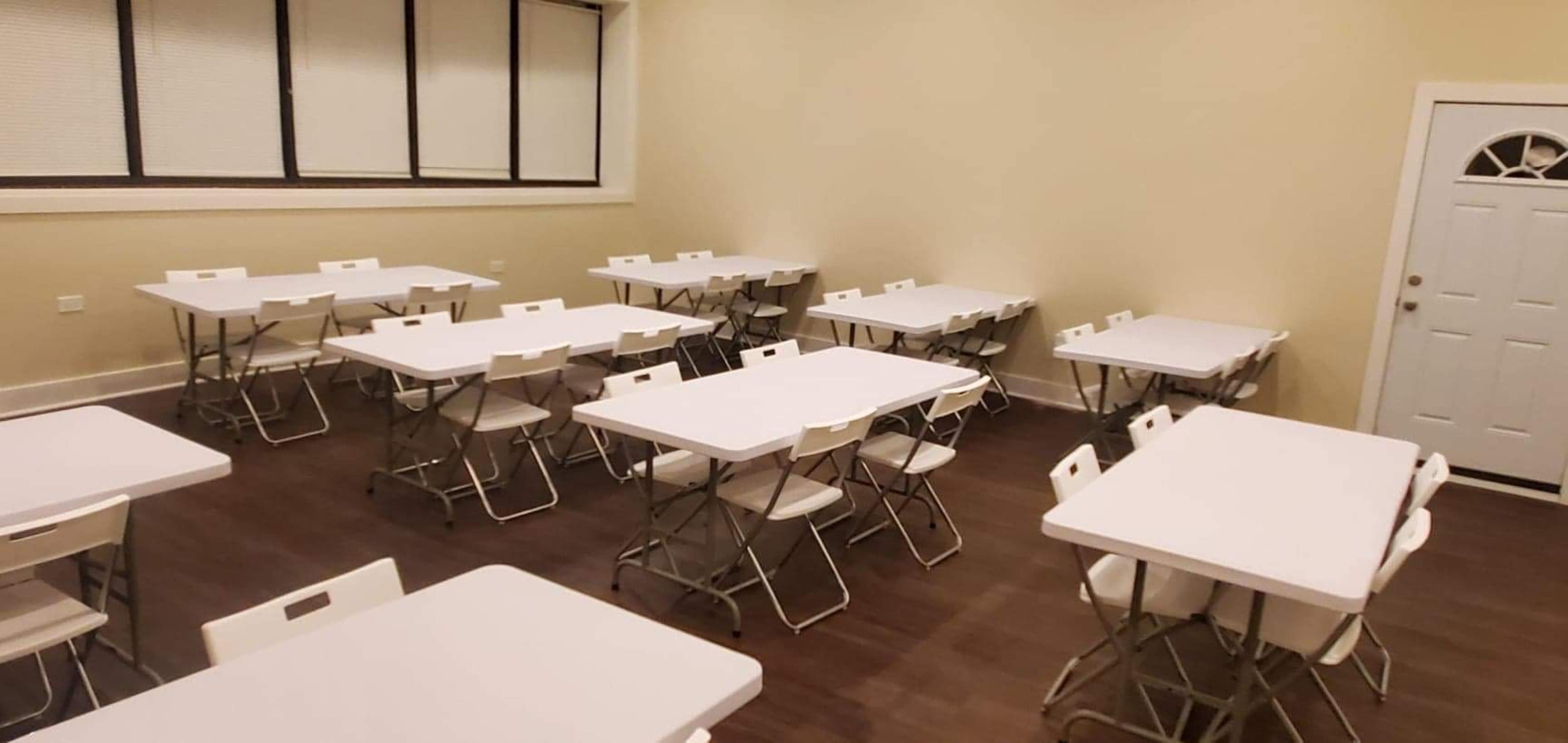 A room with multiple folding tables and chairs arranged in a grid pattern, along with a door on one side.