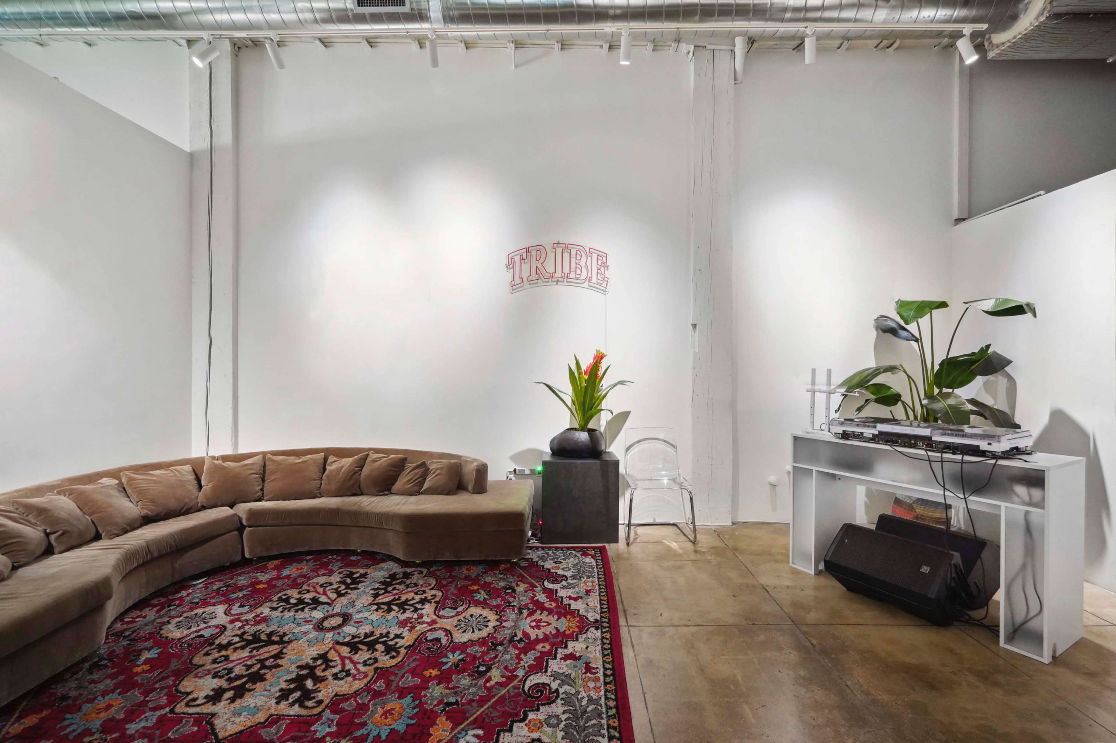 A modern, minimalist interior featuring a curved beige couch, a patterned area rug, a potted plant, and a small table with a record player against a white wall.