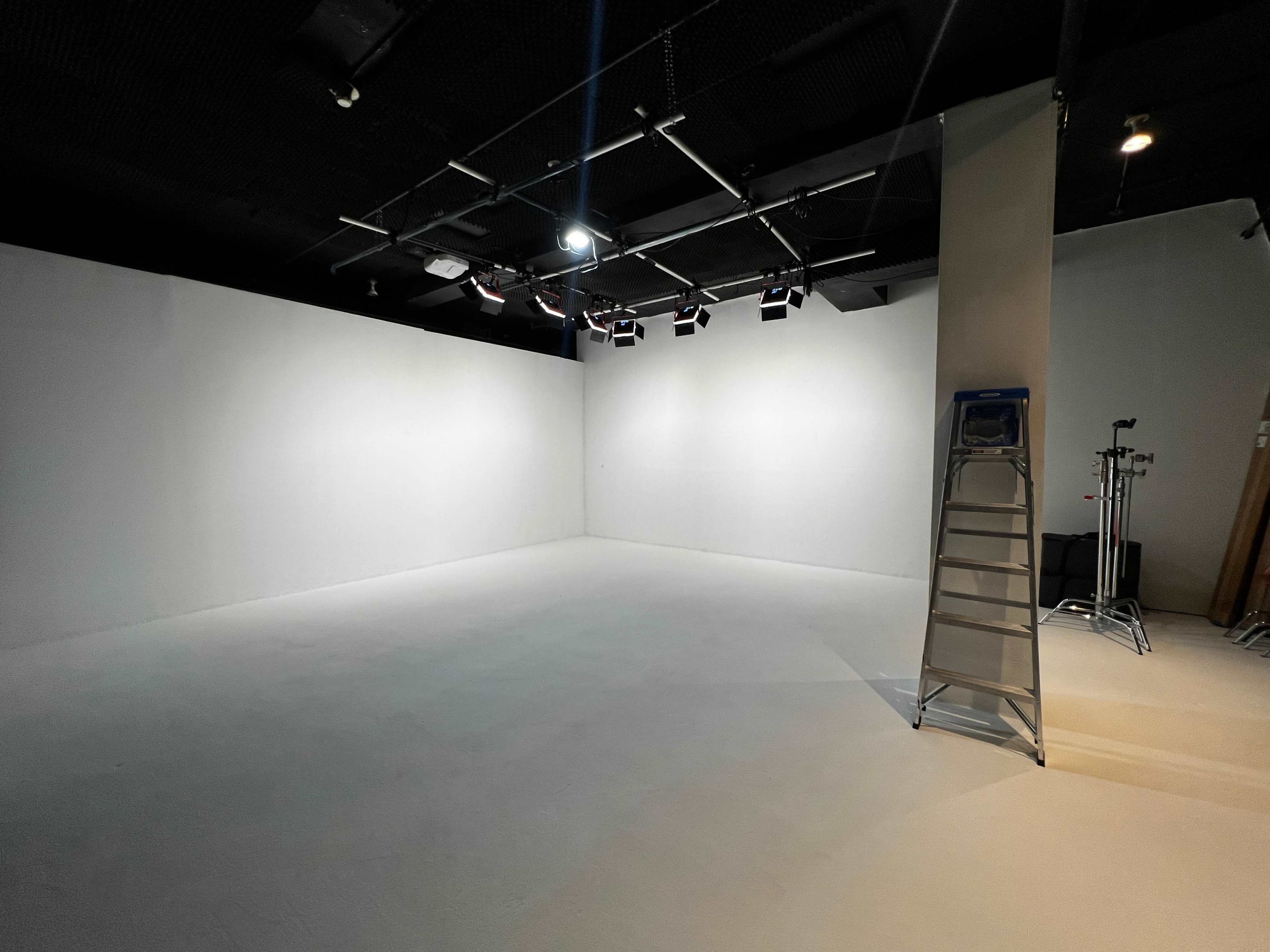A minimalist studio space with white walls, a flat white floor, and several overhead lights.