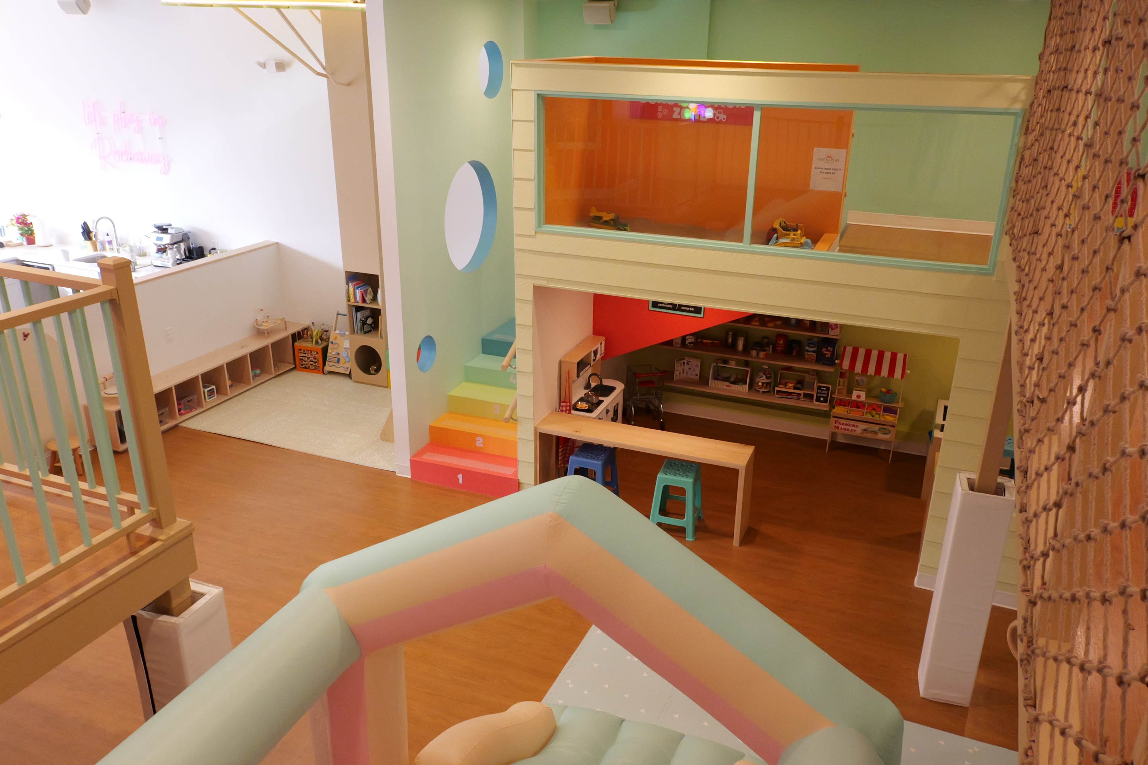 The image shows an indoor play area featuring colorful walls, a slide, and various toys and activity stations.