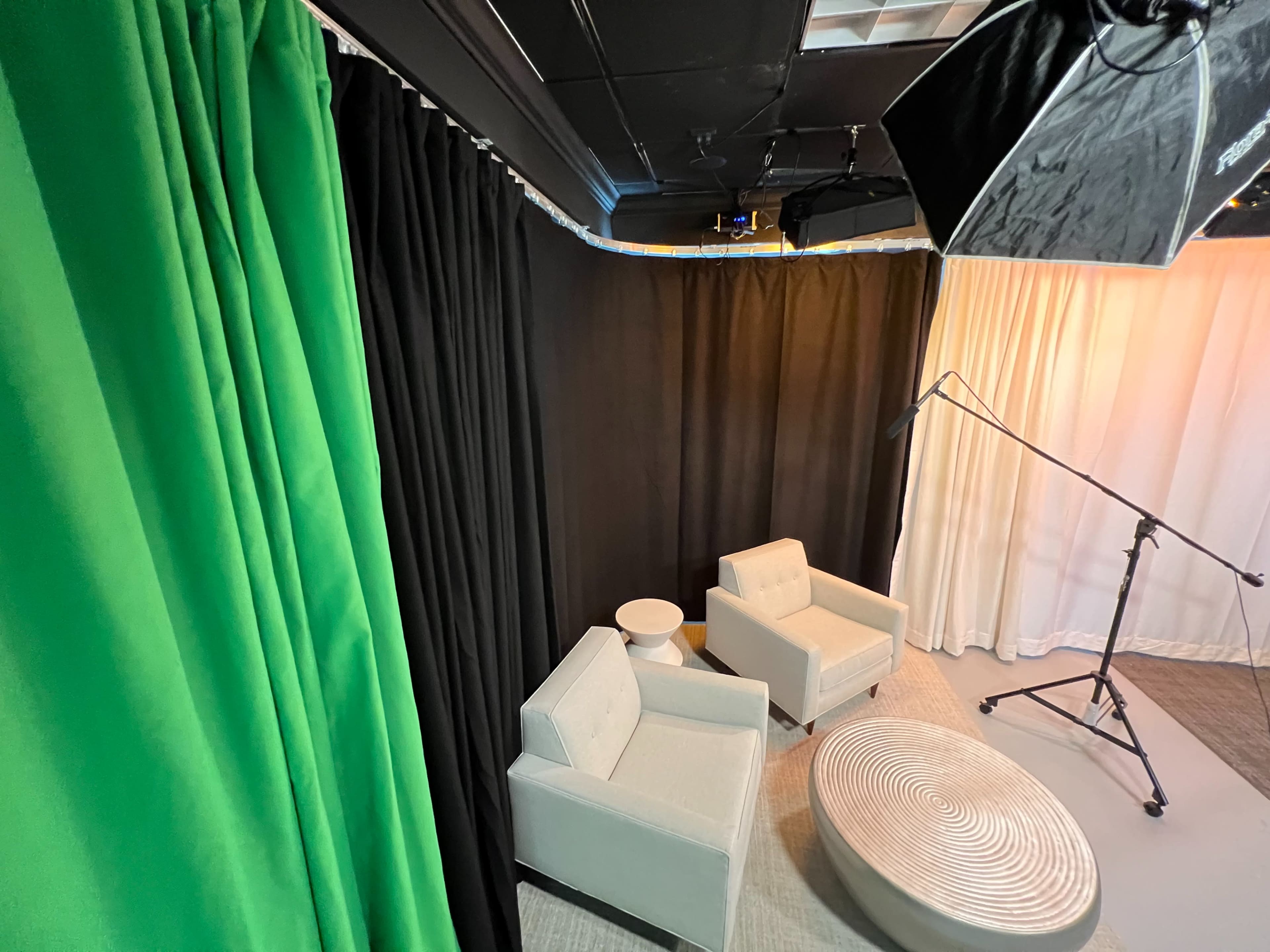 Two light gray chairs positioned near a round white table against a backdrop of green, black, and white curtains in a studio setting.