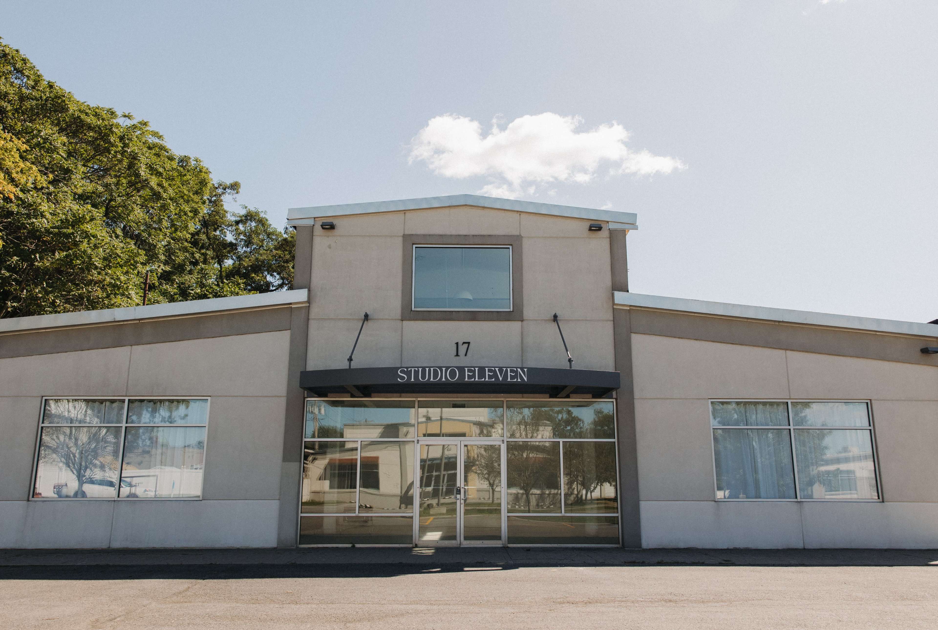 The image shows a modern, rectangular building with large glass windows and a sign that reads "STUDIO ELEVEN" above the entrance.
