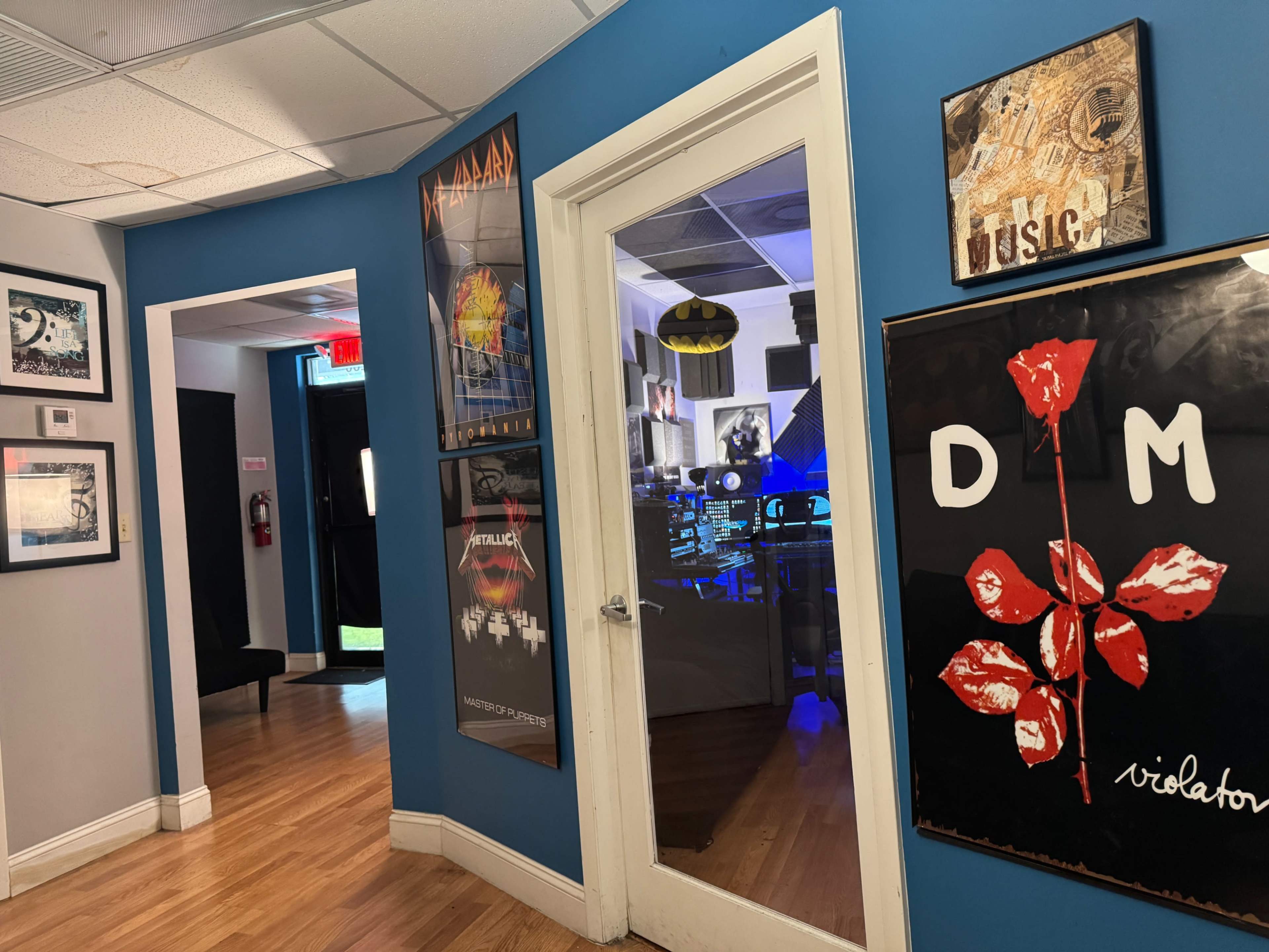 The image shows a hallway with blue walls adorned with art and music posters, leading to a room with dim lighting and visible music equipment.