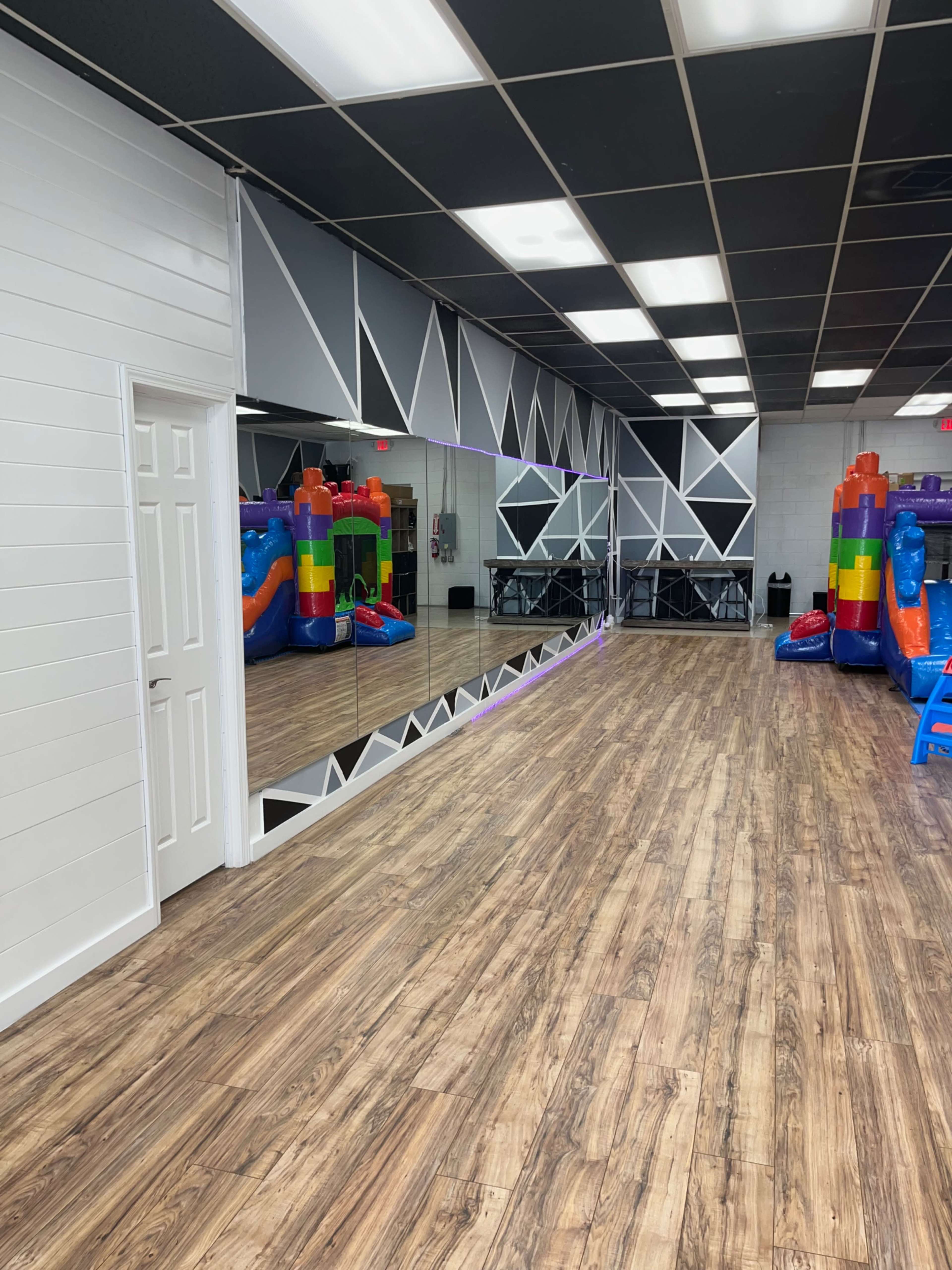 A spacious indoor area with wooden flooring, featuring a large mirror on one wall and inflatable play structures in vibrant colors on the right side.