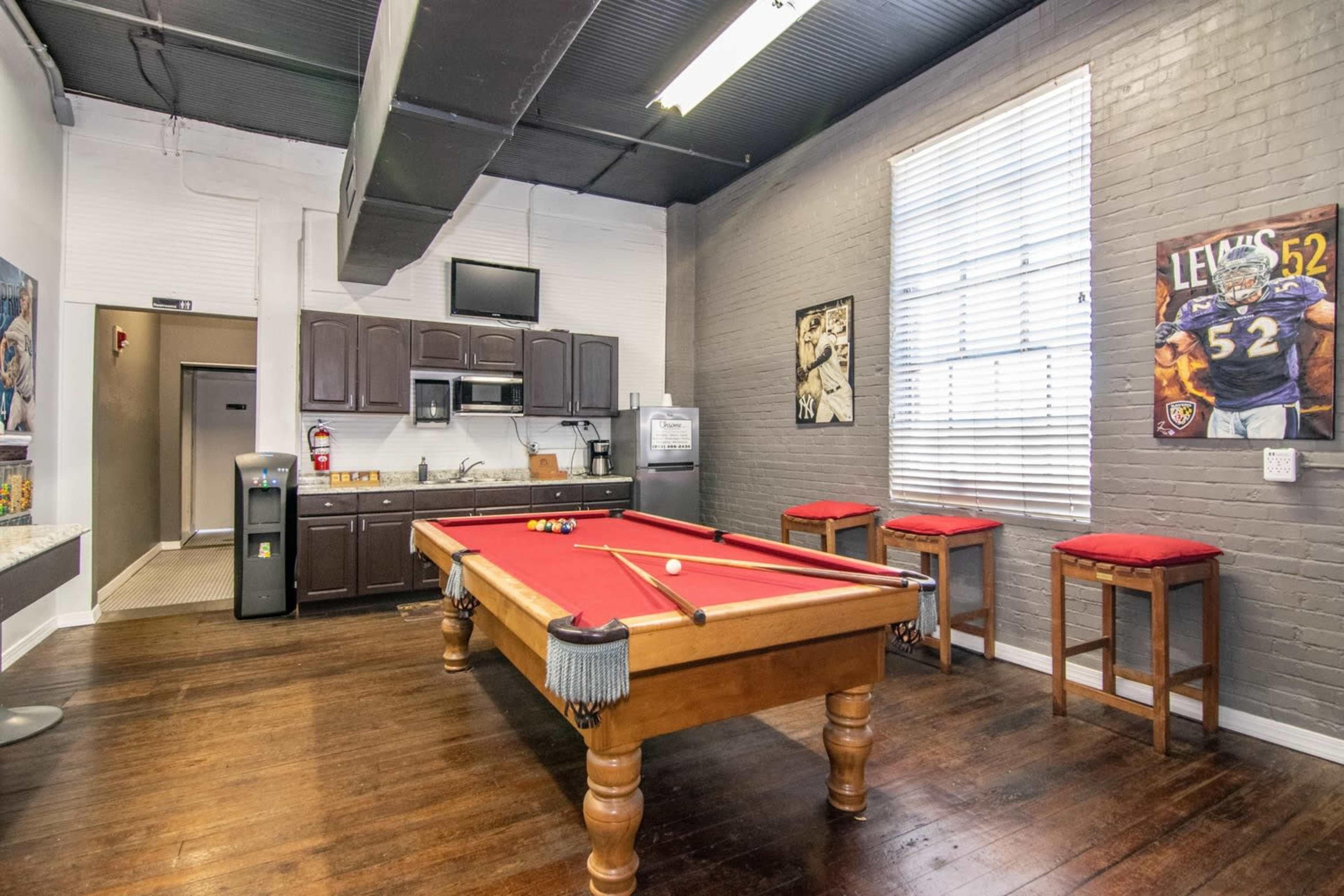 A recreational room with a pool table, kitchenette, and bar stools against brick walls.