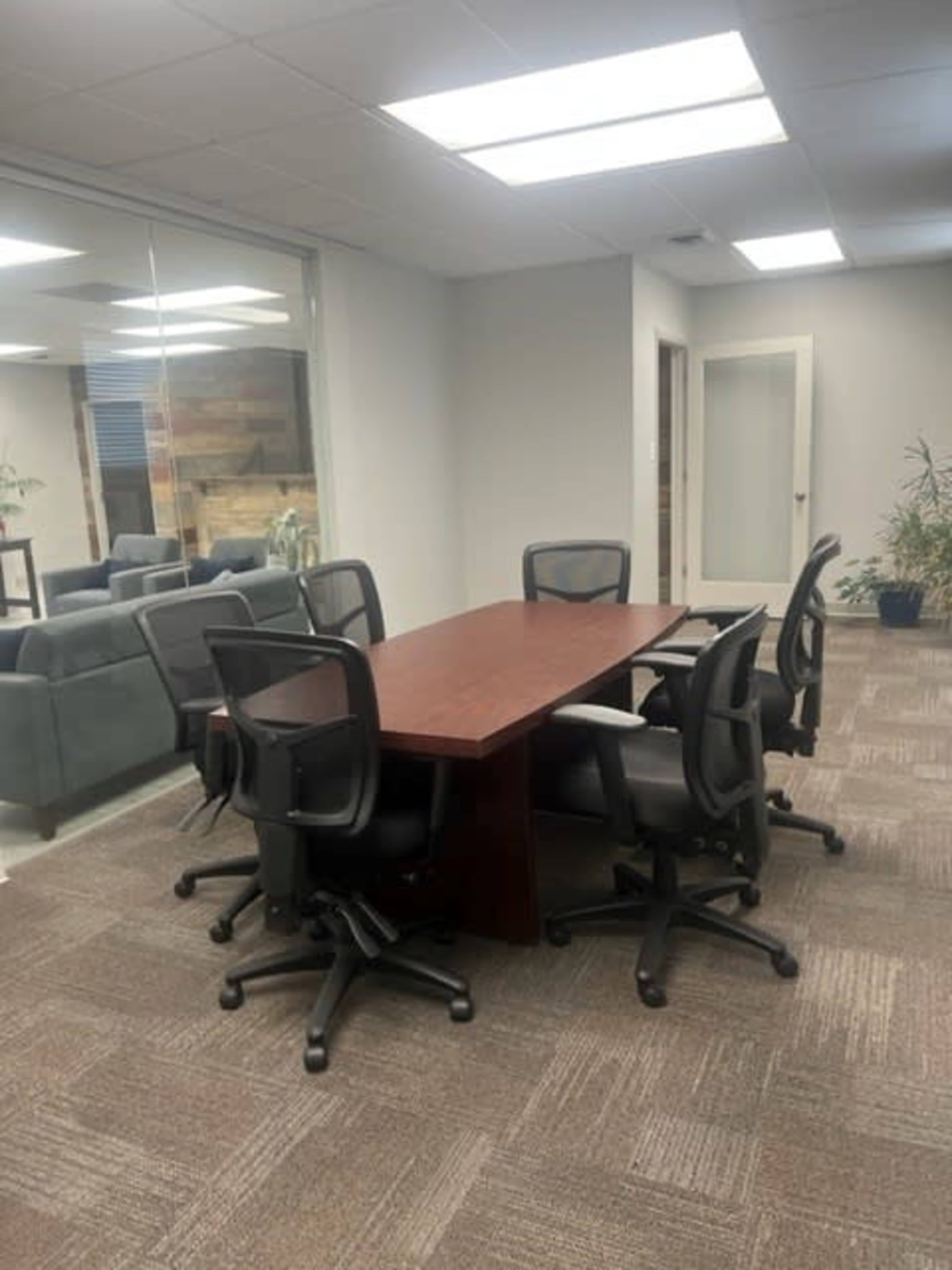 A conference room features a rectangular wooden table surrounded by six black rolling chairs.