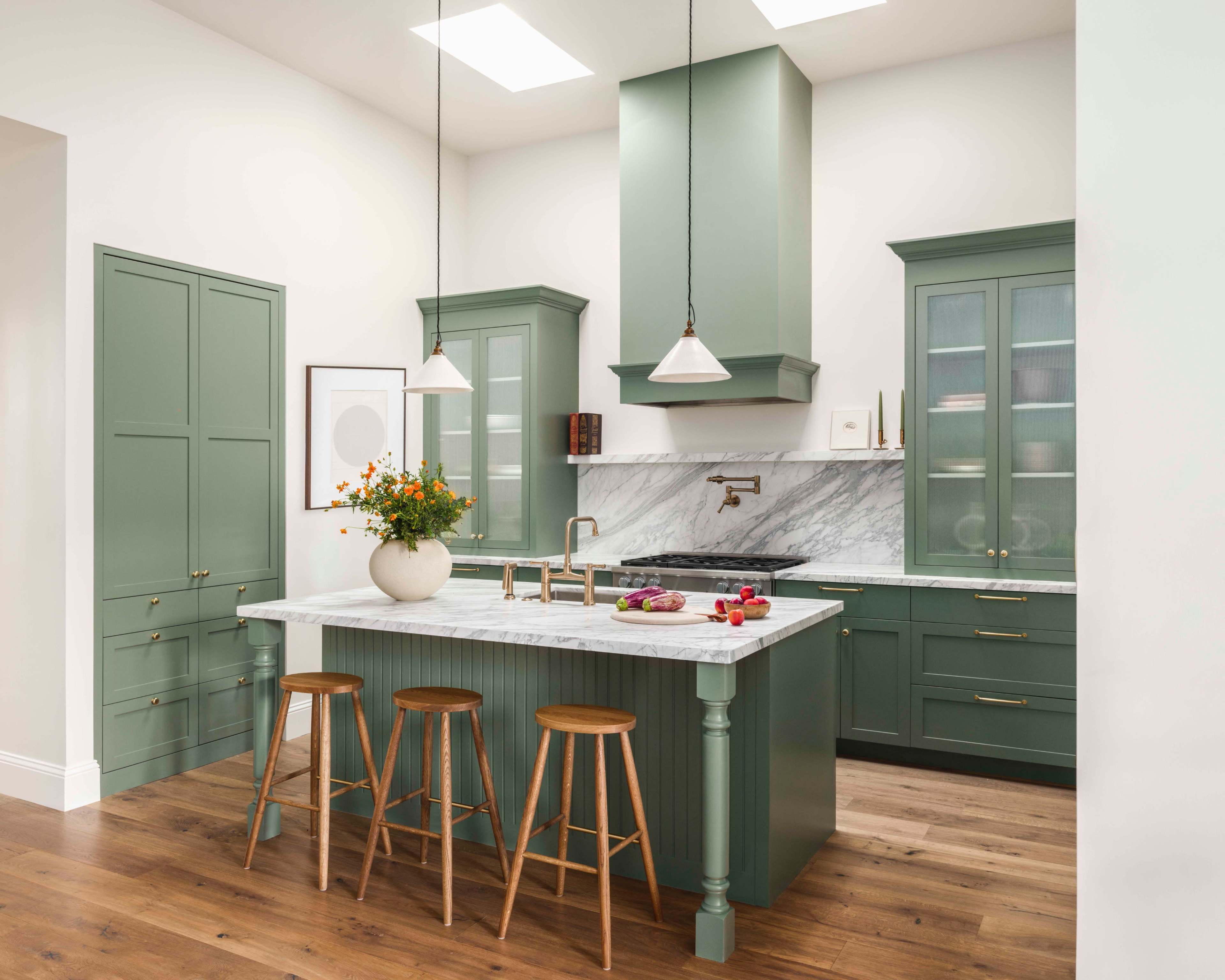 The kitchen features green cabinetry, a marble countertop island with three wooden stools, and overhead light fixtures.