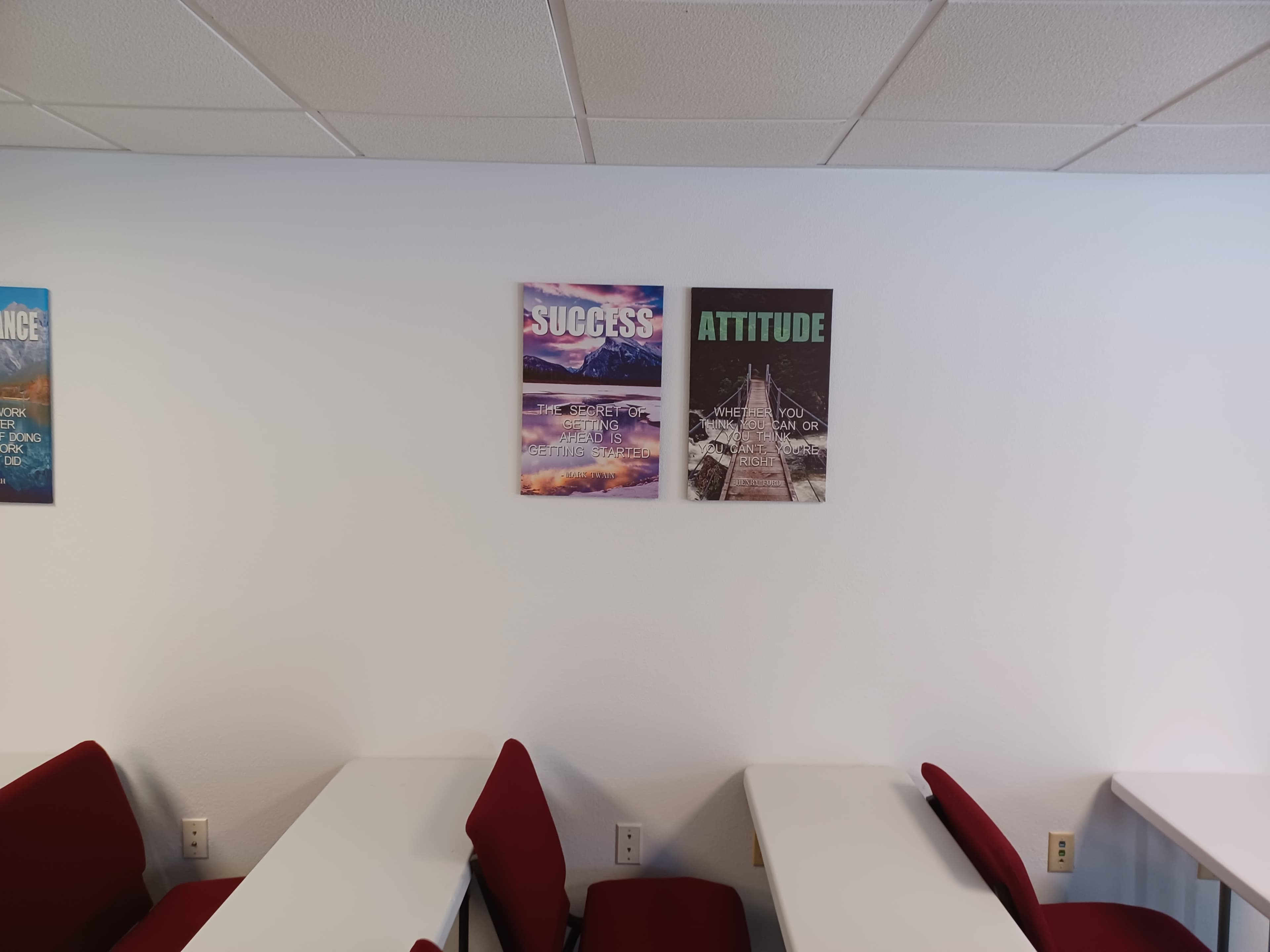 The image shows a wall in a classroom with two motivational posters, one displaying the word "SUCCESS" and the other "ATTITUDE," alongside rows of empty desks with red chairs.